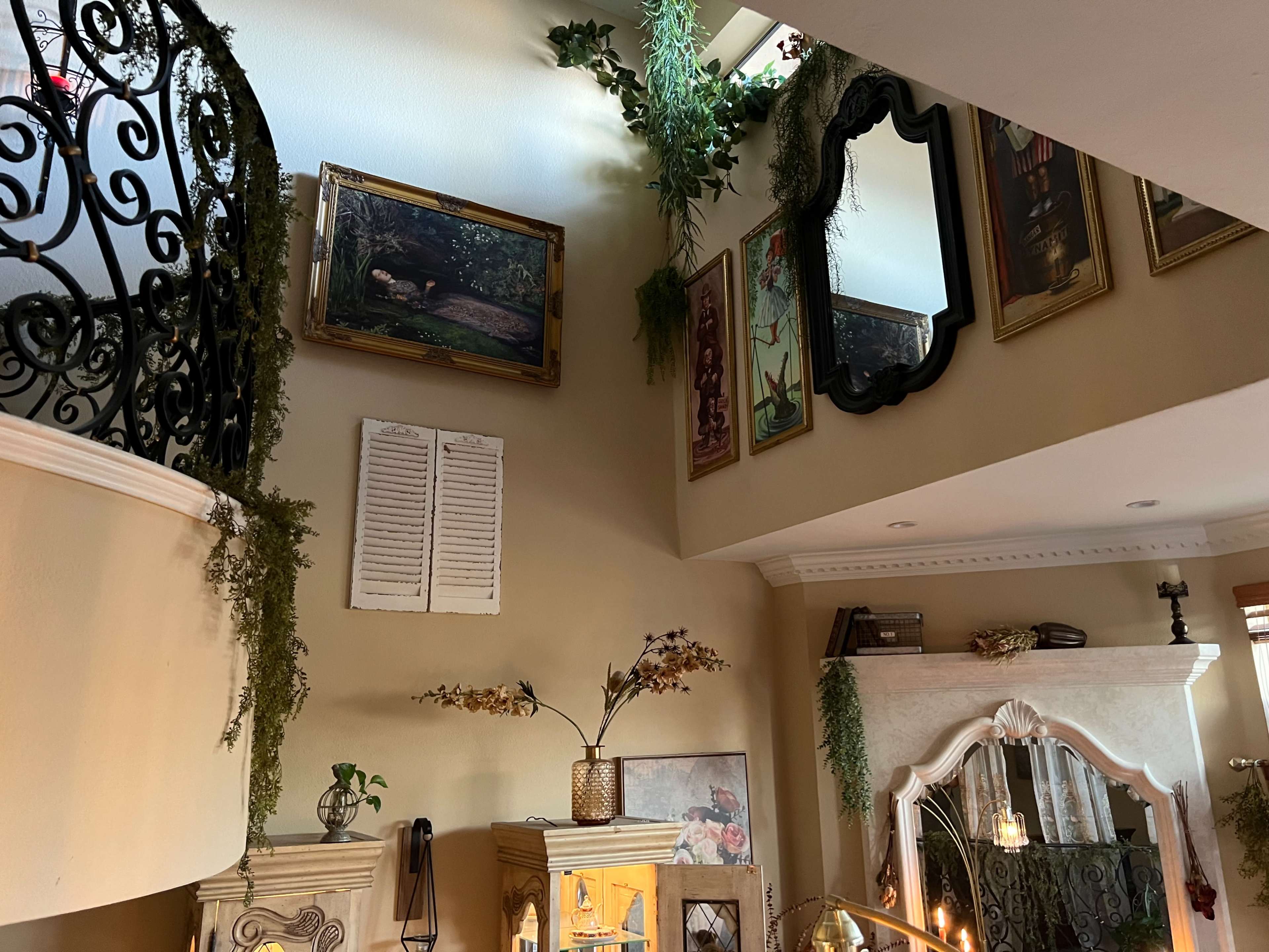 An interior space with a staircase, adorned walls featuring various framed artworks and mirrors, and decorative plants.
