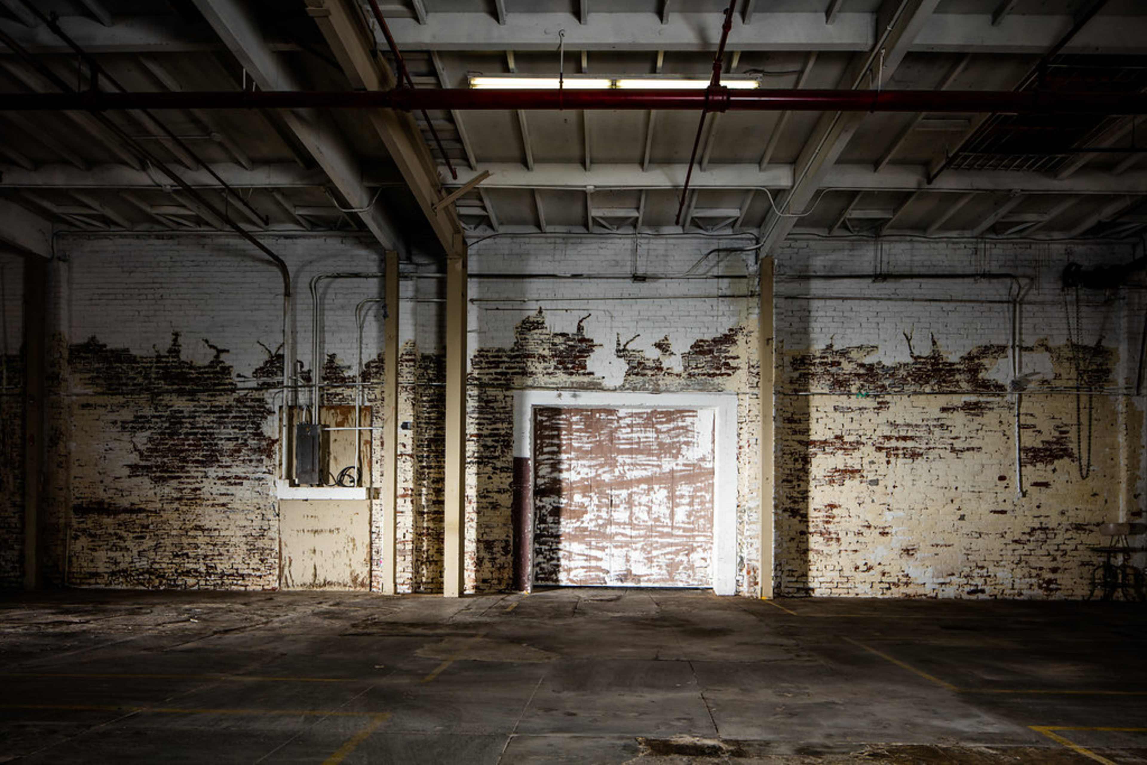 An empty industrial space with peeling white paint and an open doorway revealing a wooden door.