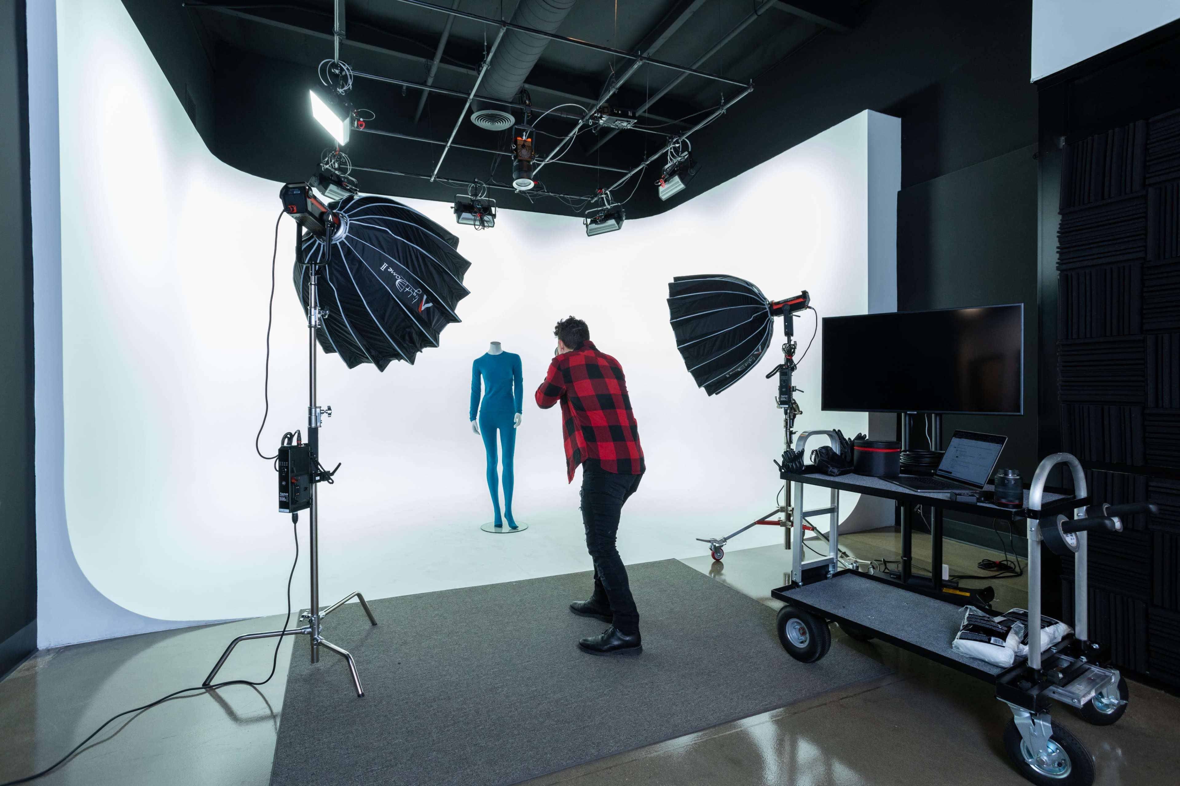 A photographer adjusts lighting equipment in a studio featuring a backdrop and a mannequin.