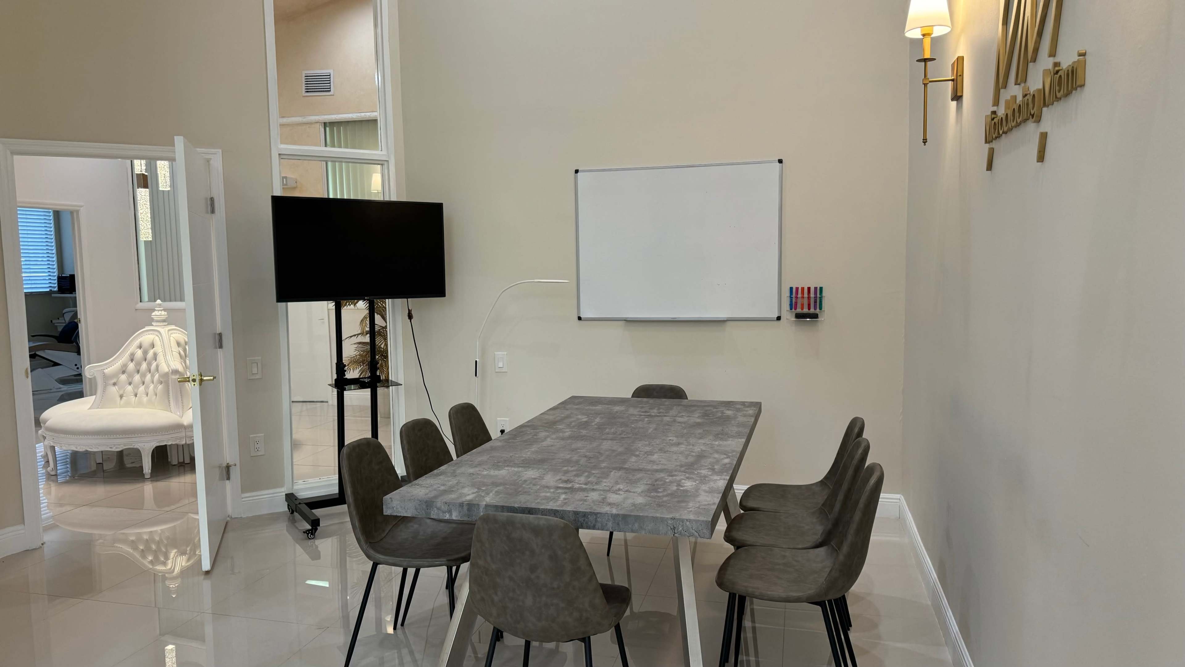 The image shows a modern meeting room with a rectangular table surrounded by eight chairs, a whiteboard on the wall, and a television on a stand.