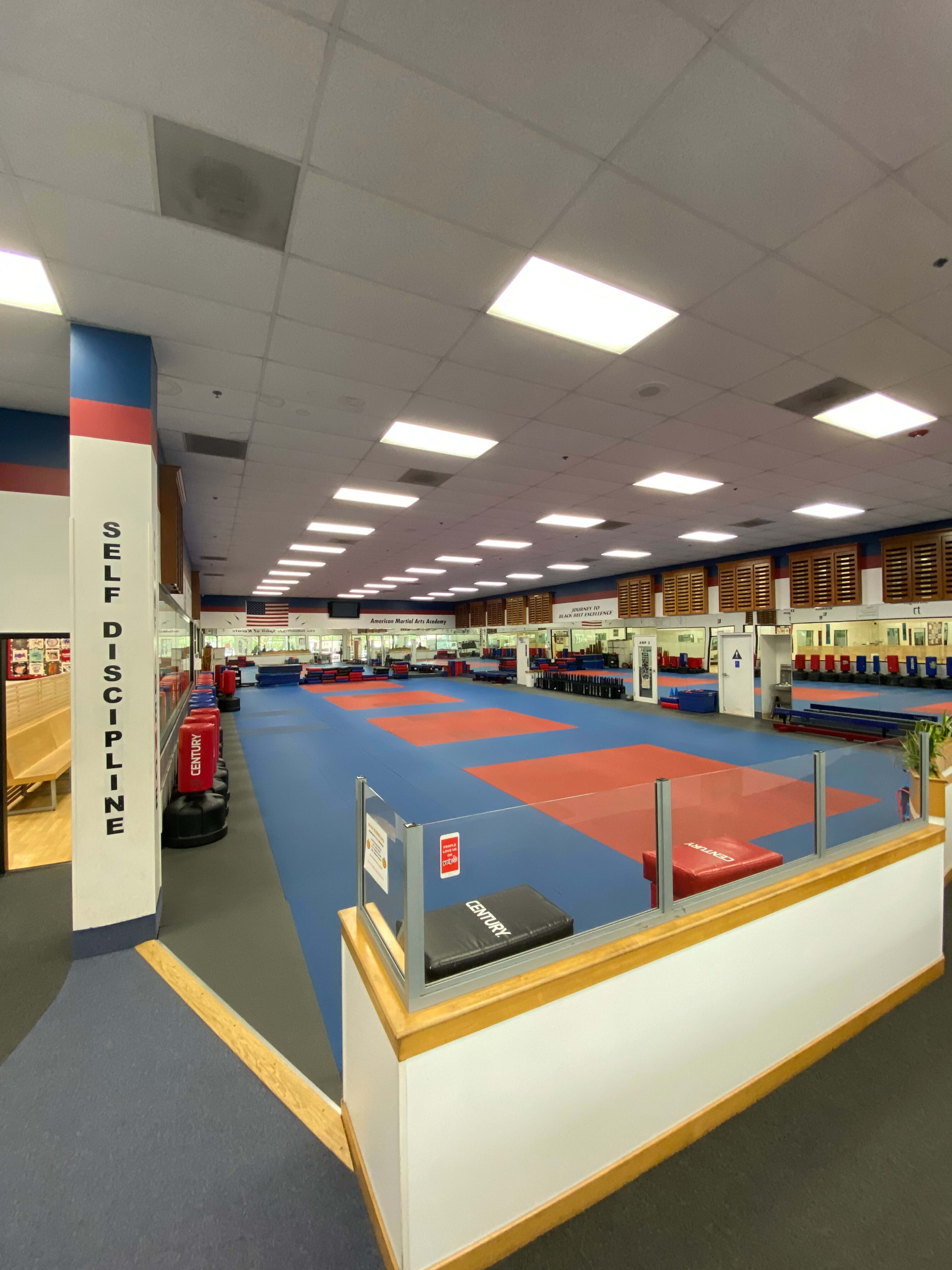 The image shows a spacious martial arts training studio with colored mats and training equipment arranged systematically.