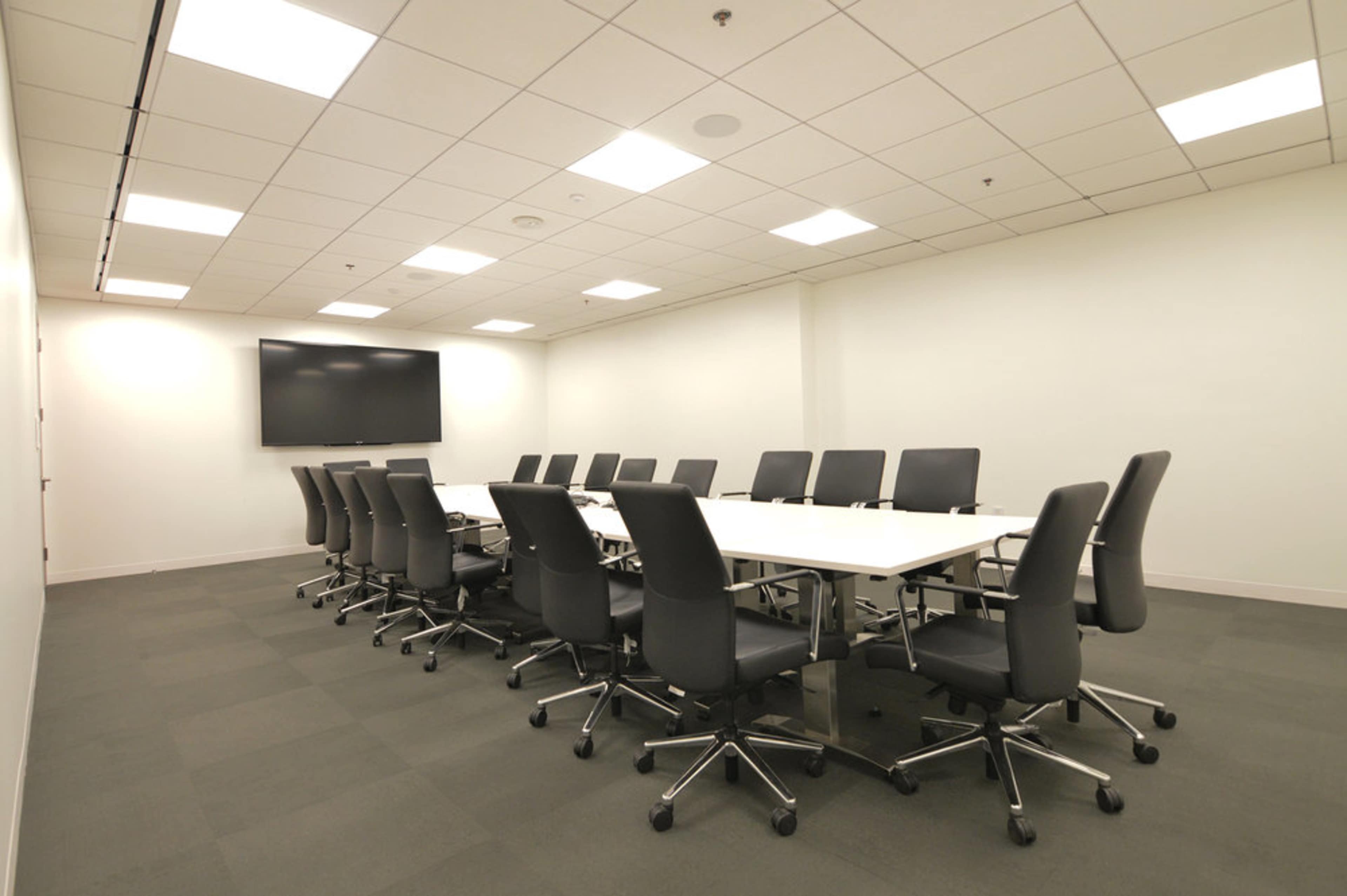 A conference room features a long table surrounded by office chairs and a large television mounted on the wall.