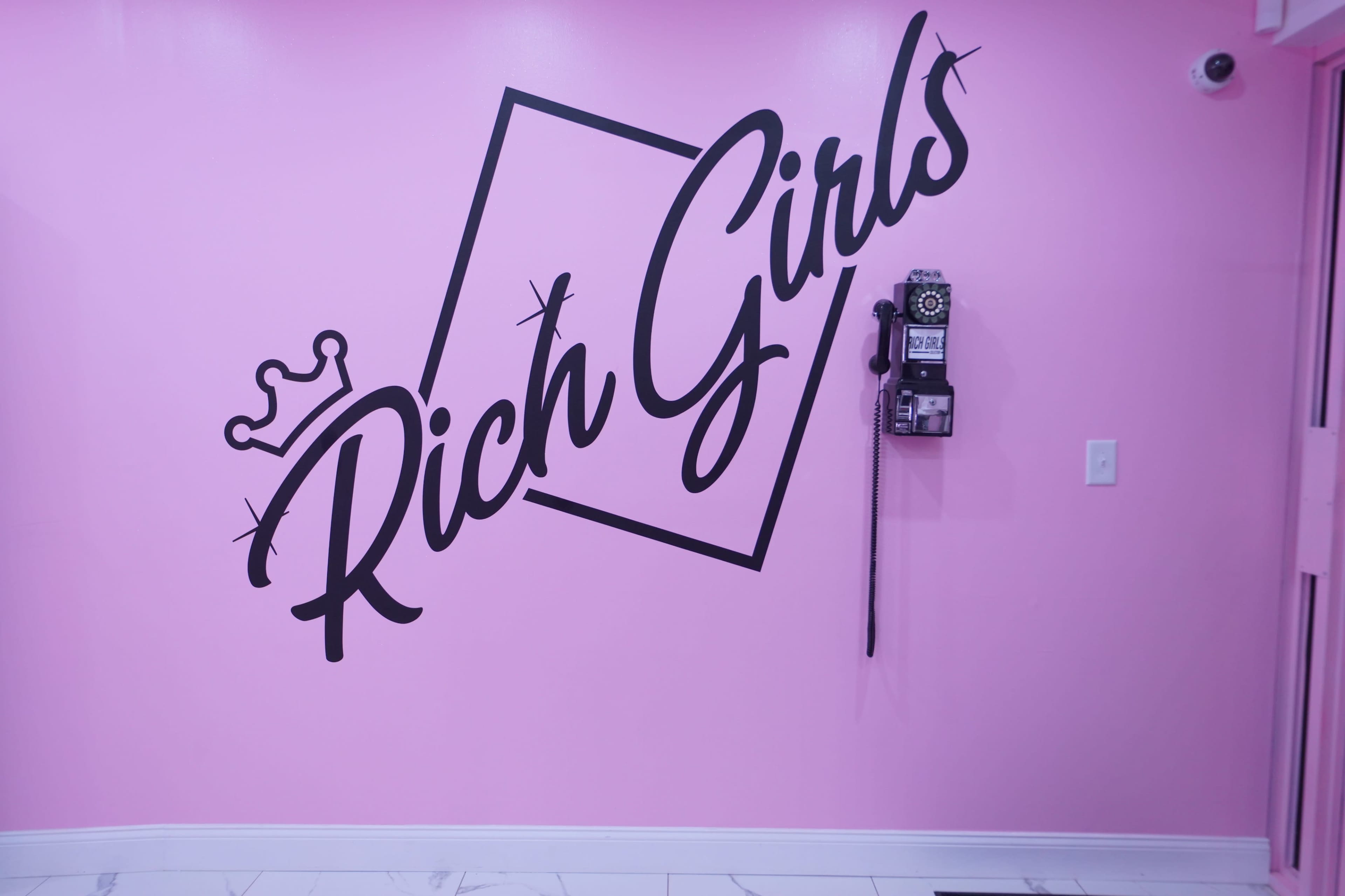 A pink wall features the words "Rich Girls" in bold, stylized lettering next to a vintage telephone.