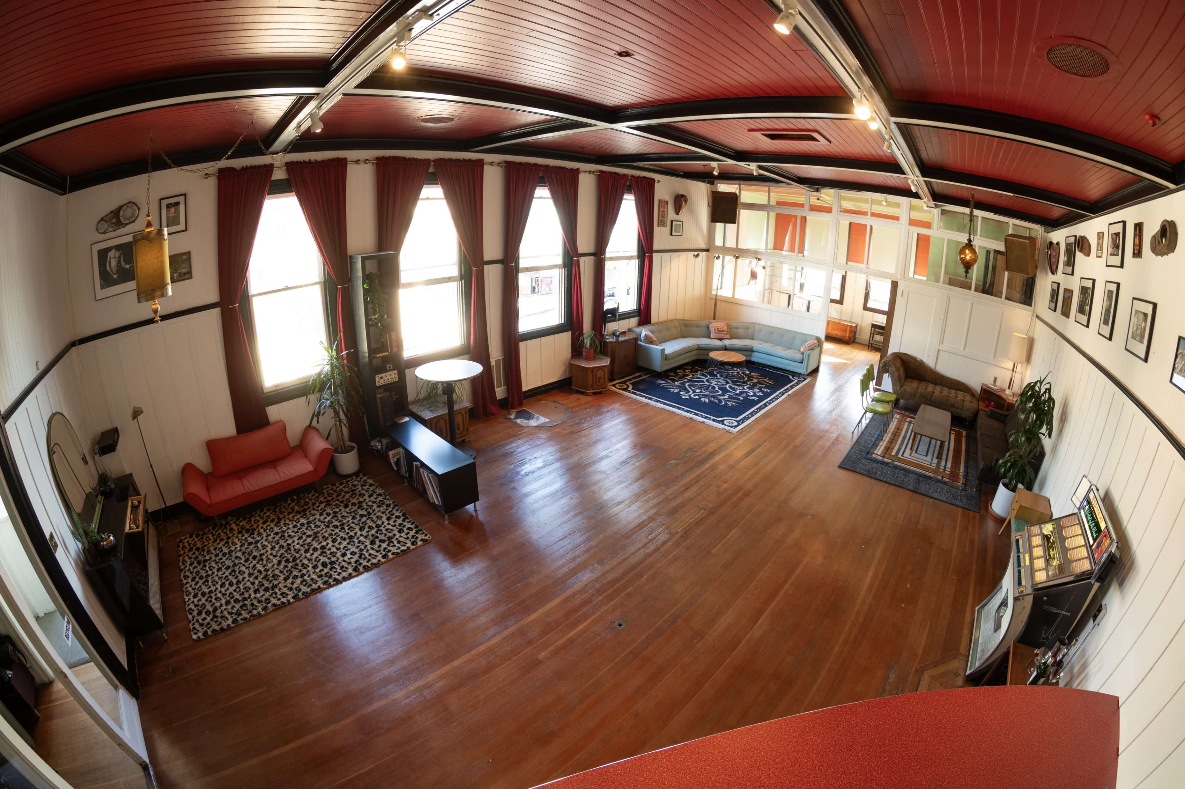 A spacious room with wooden floors, various seating areas, large windows, and decorative elements on the walls.