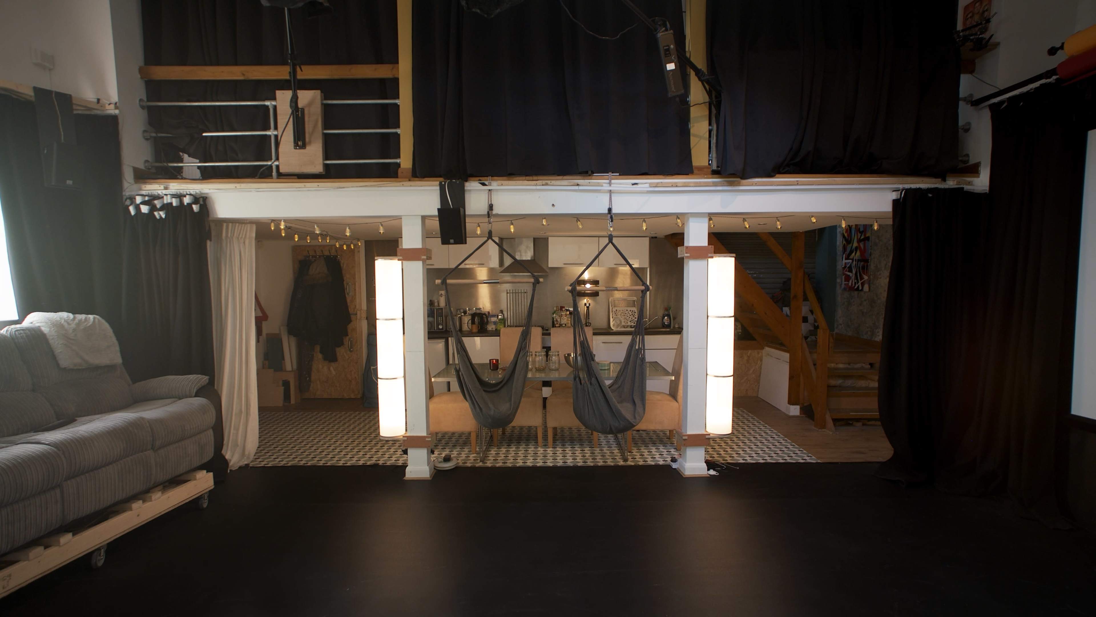 A spacious studio with two hammocks suspended between light columns, a kitchenette in the background, and a gray sofa to the left.