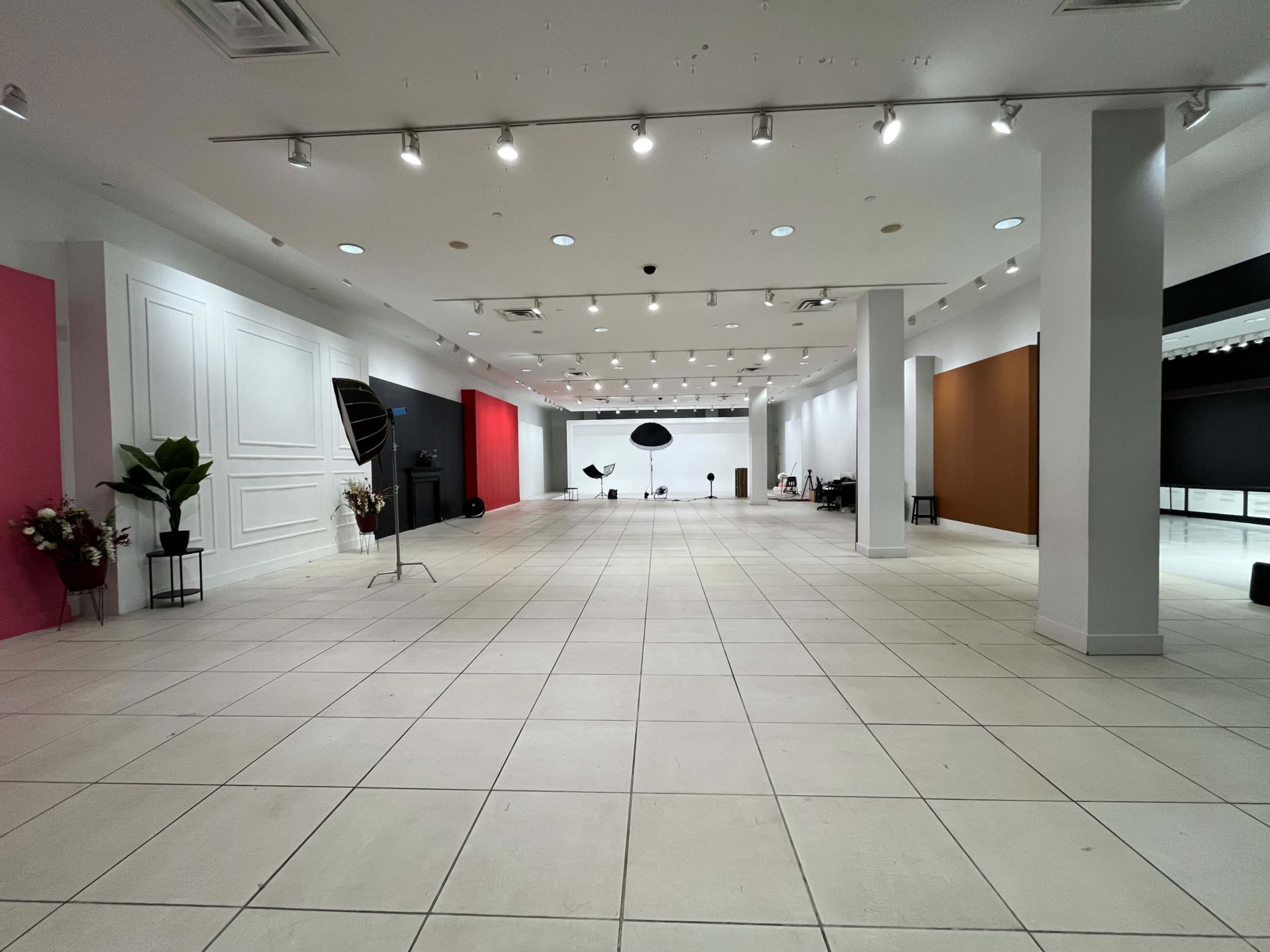 The image shows a spacious, empty indoor studio with various colored backdrops and professional lighting equipment set up along the walls.