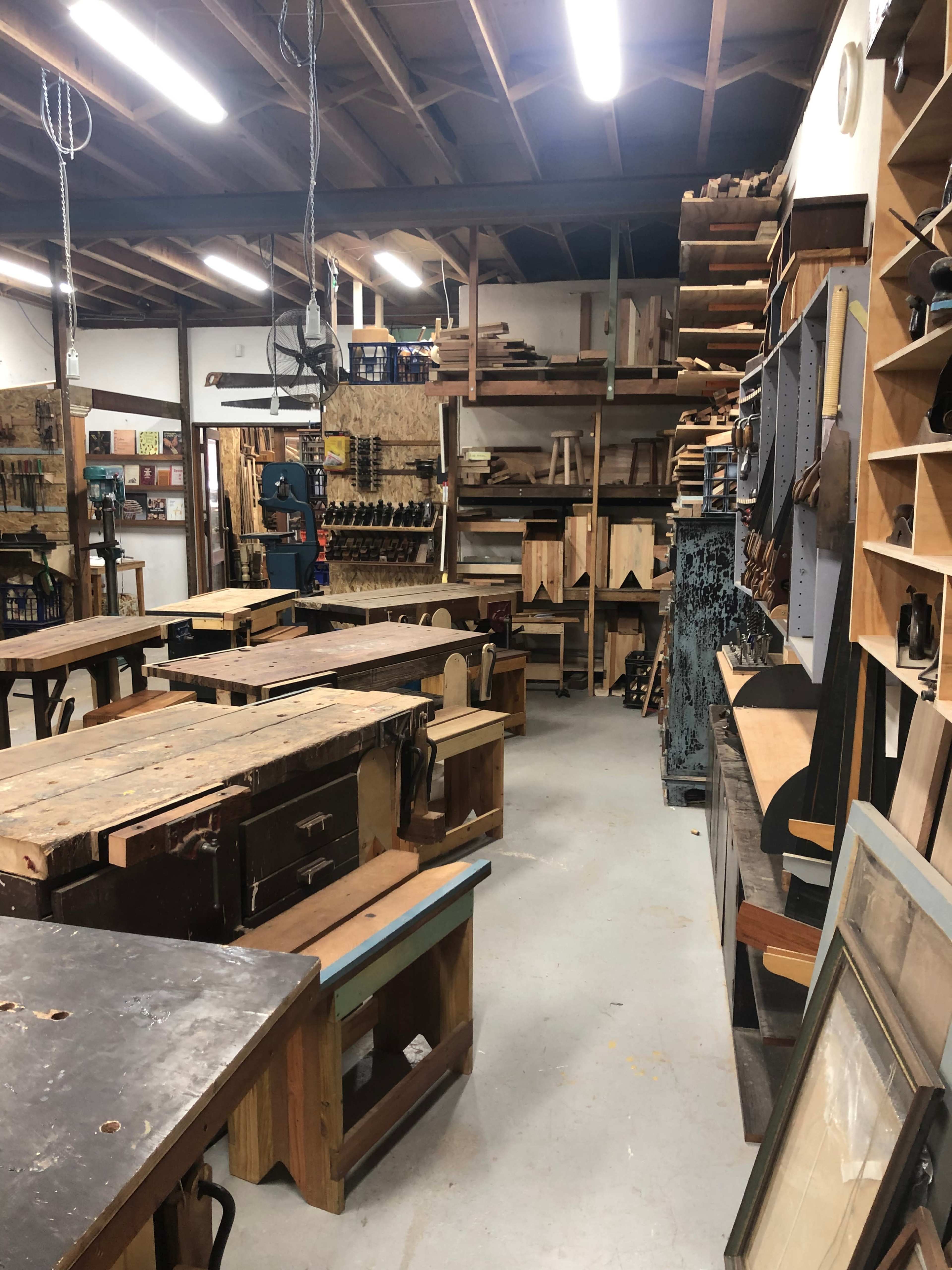 A woodworking shop with various tools and materials organized on shelves and worktables.