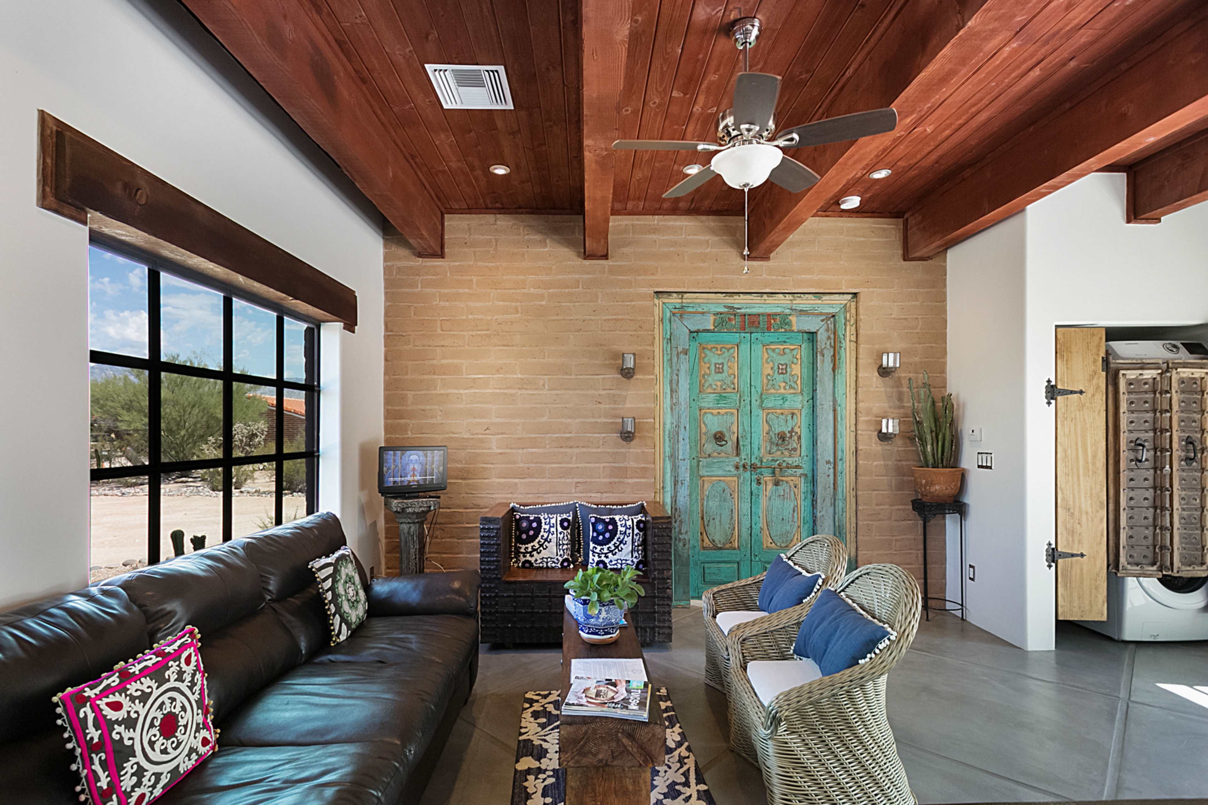 A living room with a brown leather sofa, a wooden coffee table, and an antique teal door against a brick wall.