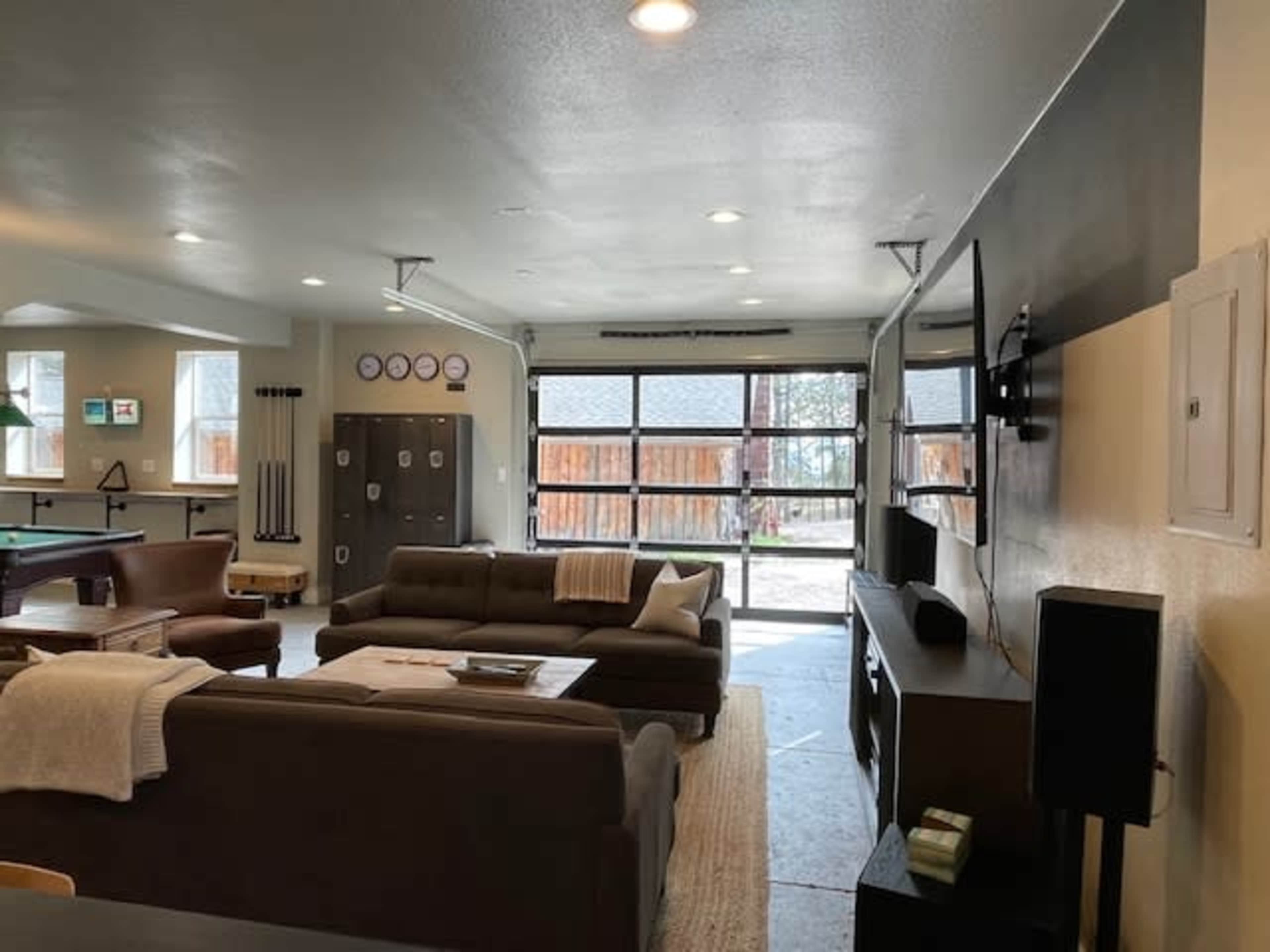 A spacious living area with a sectional sofa, a large wall-mounted TV, and a garage-style door opening to an outdoor view.