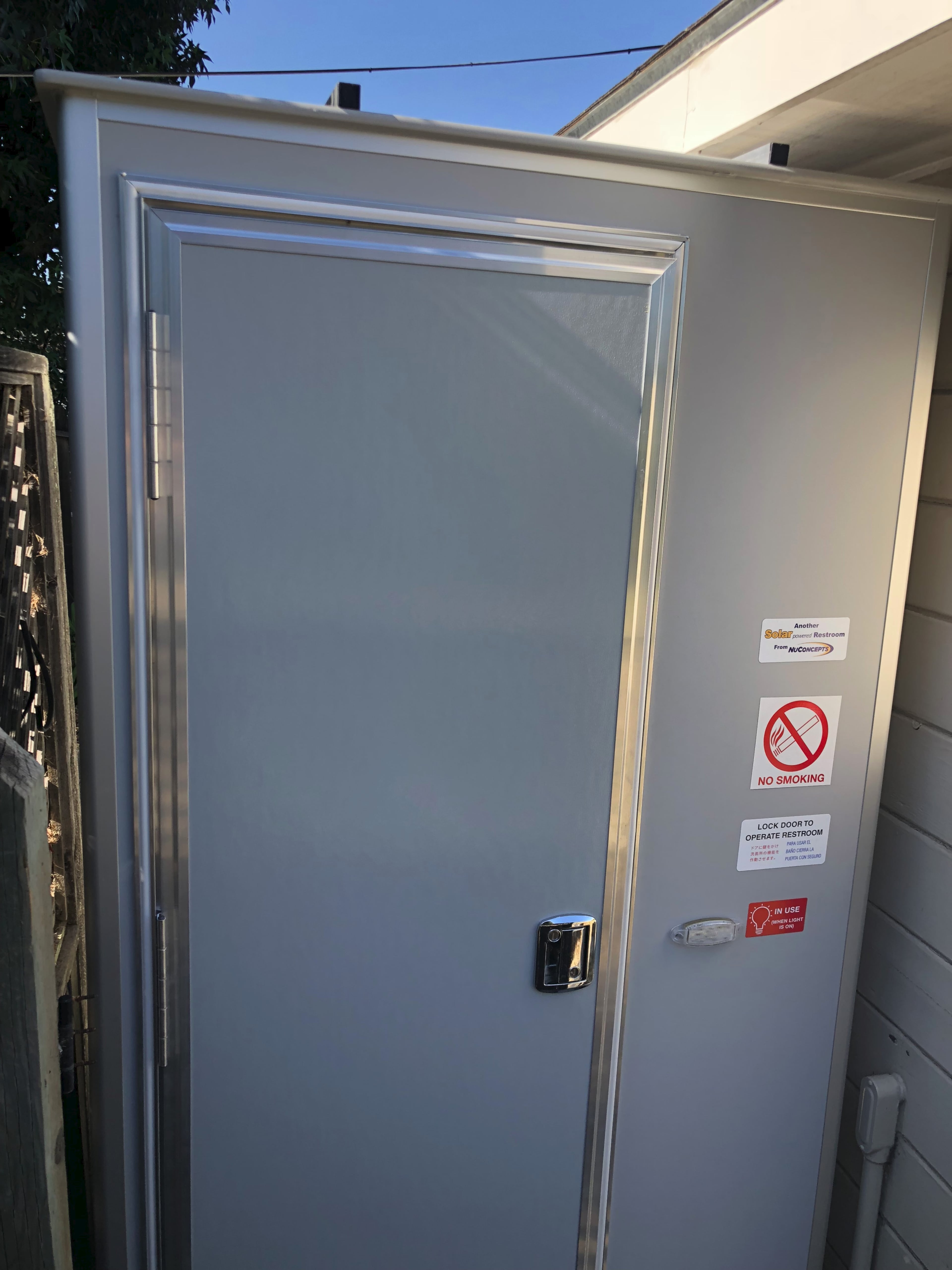 A gray metal door with a padlock and warning signs attached, set against a light-colored wall.