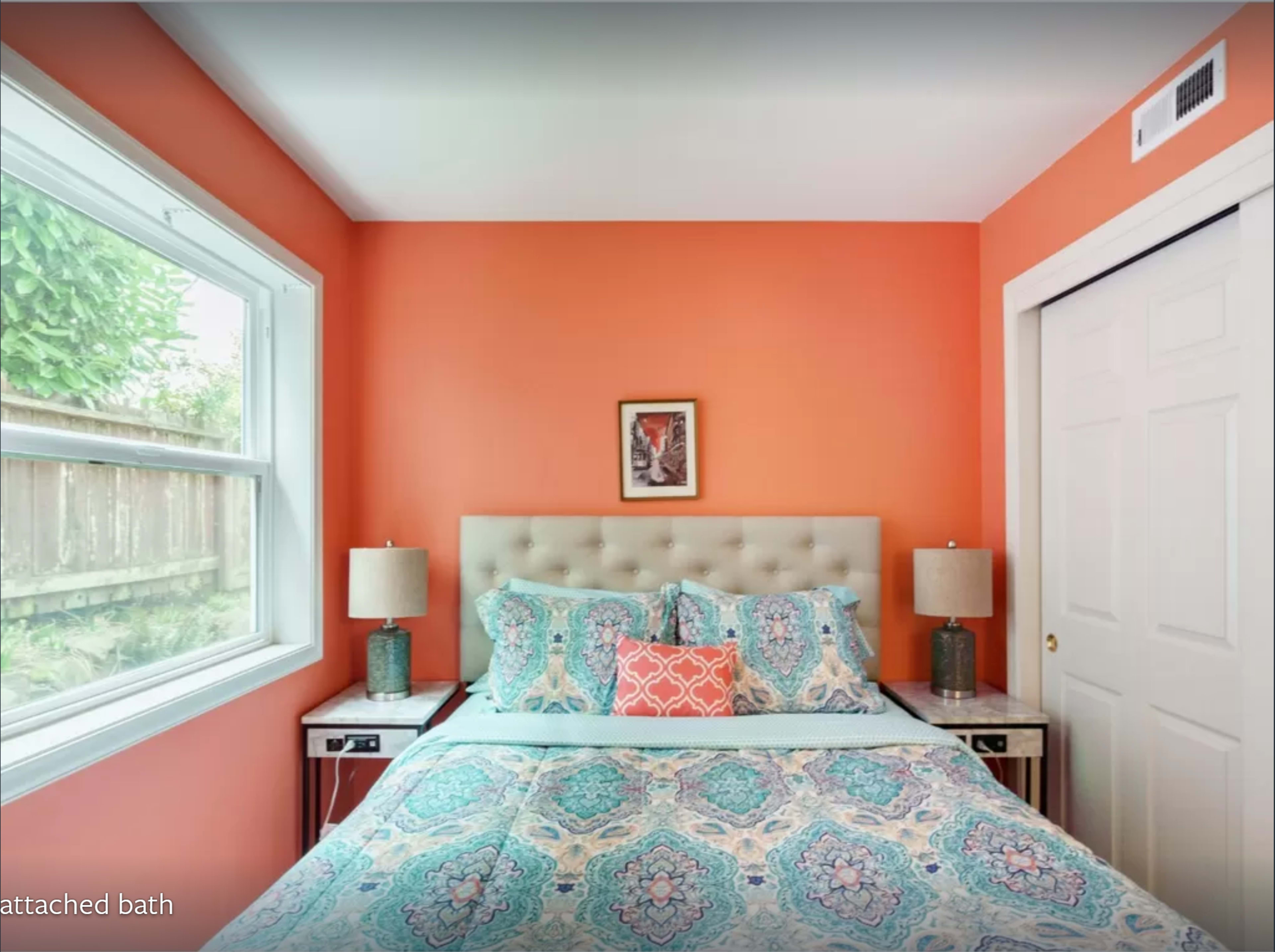 A bedroom with an orange wall, a bed covered in a patterned quilt, and two bedside tables with lamps on either side.