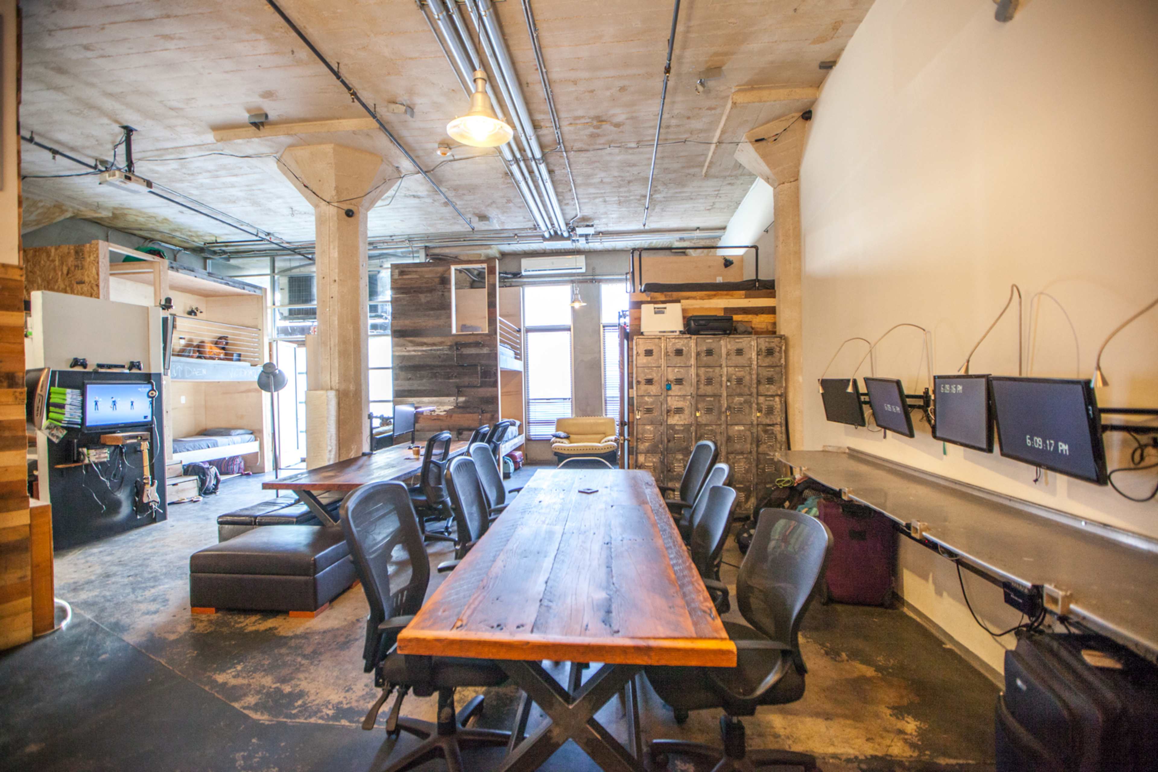 A spacious office interior featuring a large wooden table surrounded by chairs, with workstations and storage units in the background.