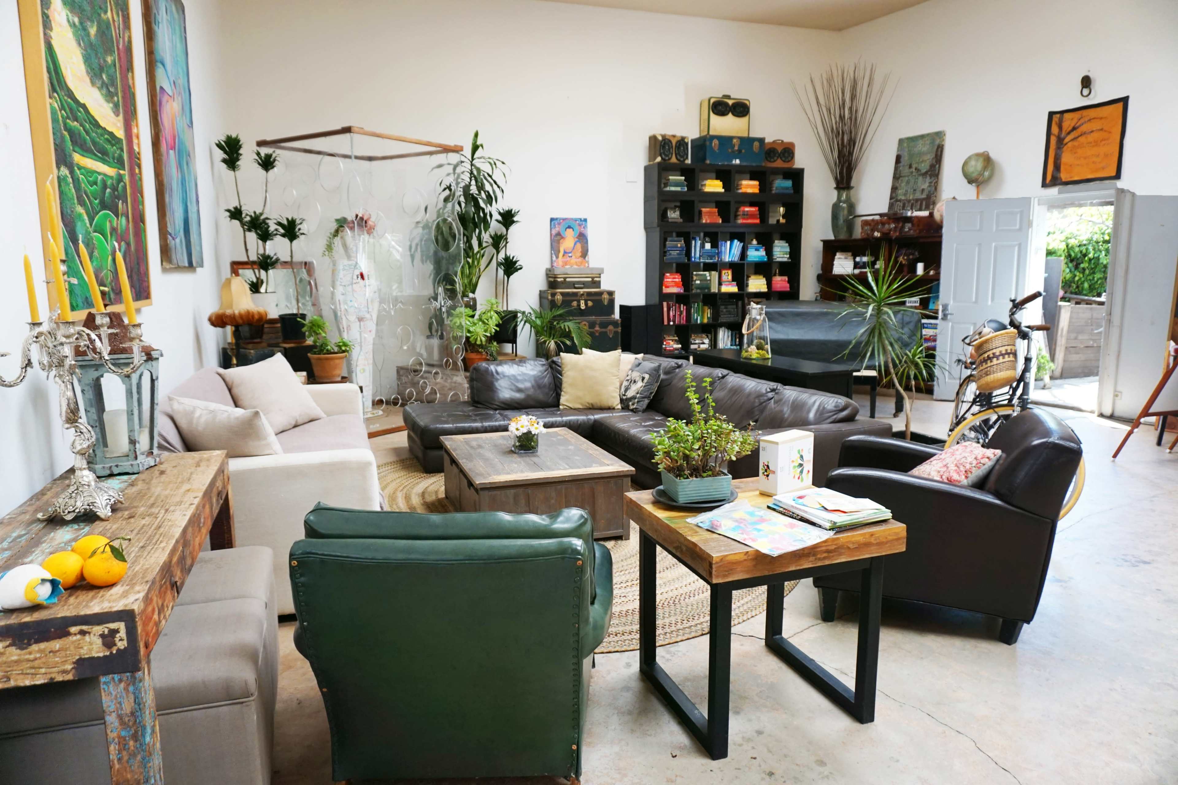 A spacious living area furnished with a mix of leather and upholstered sofas, coffee tables, plants, and shelves filled with books.