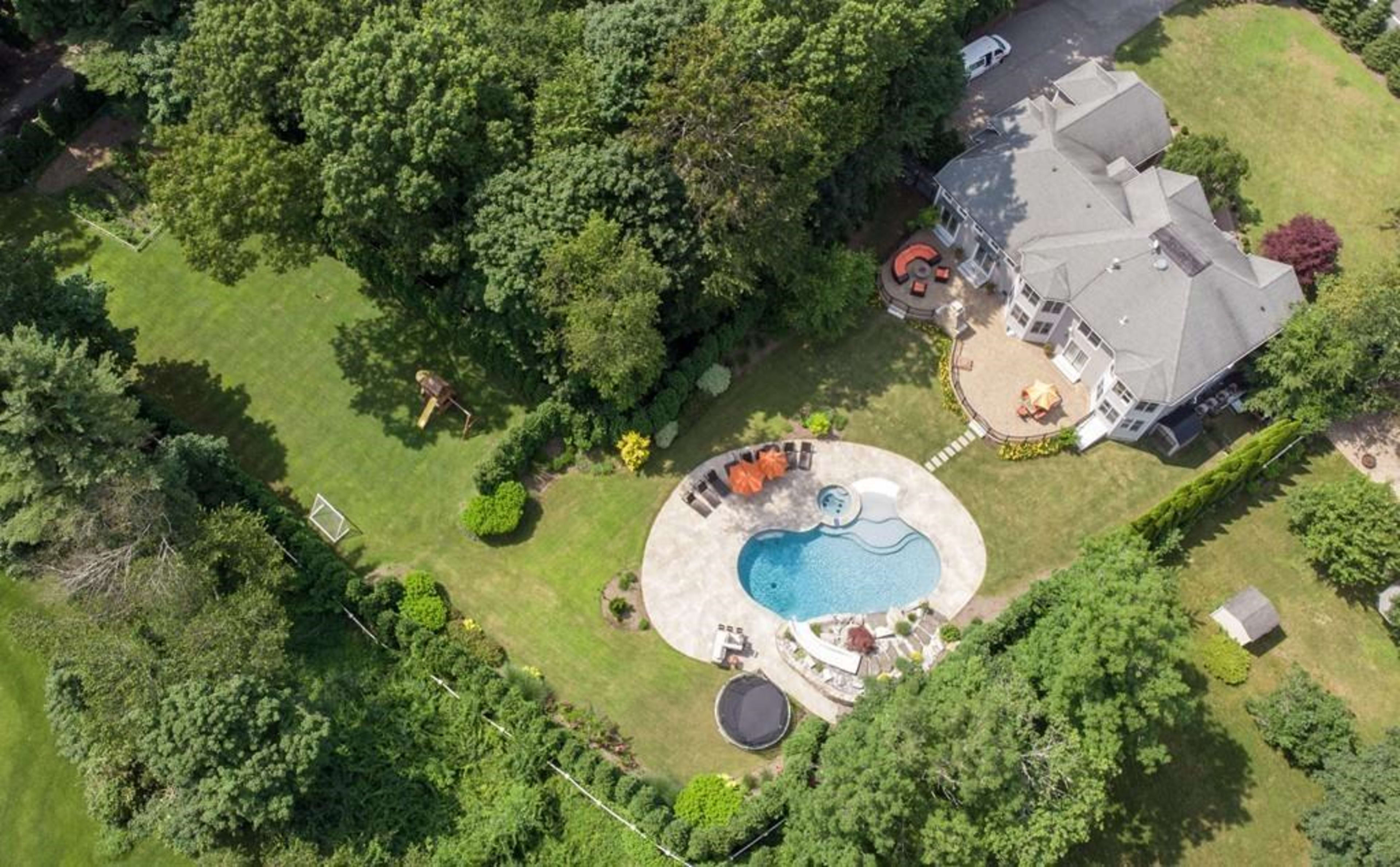 An aerial view of a large house with a swimming pool and landscaped yard surrounded by trees.