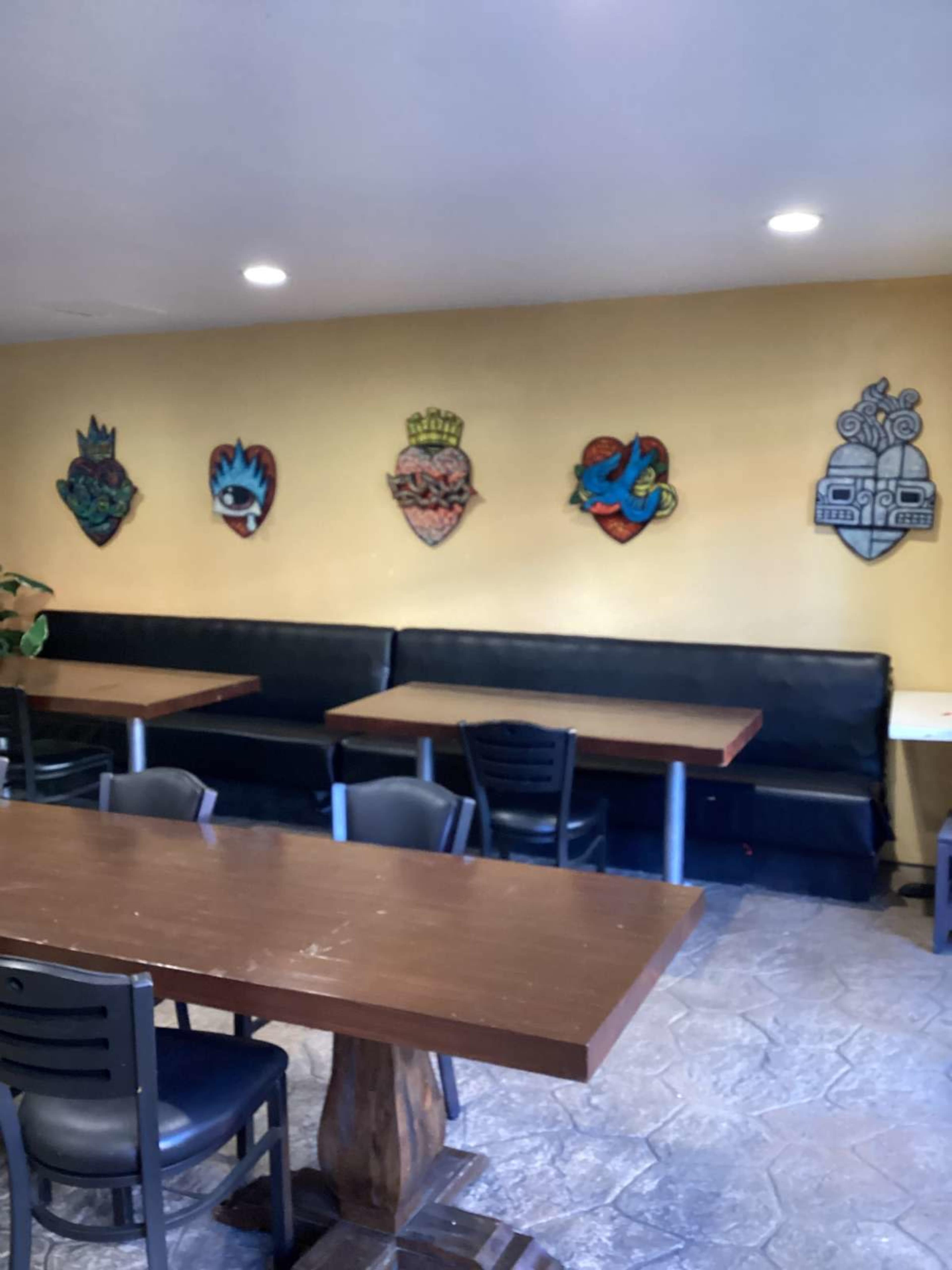 The image shows a dining area with black booths and tables, featuring colorful wall art in the form of shields.
