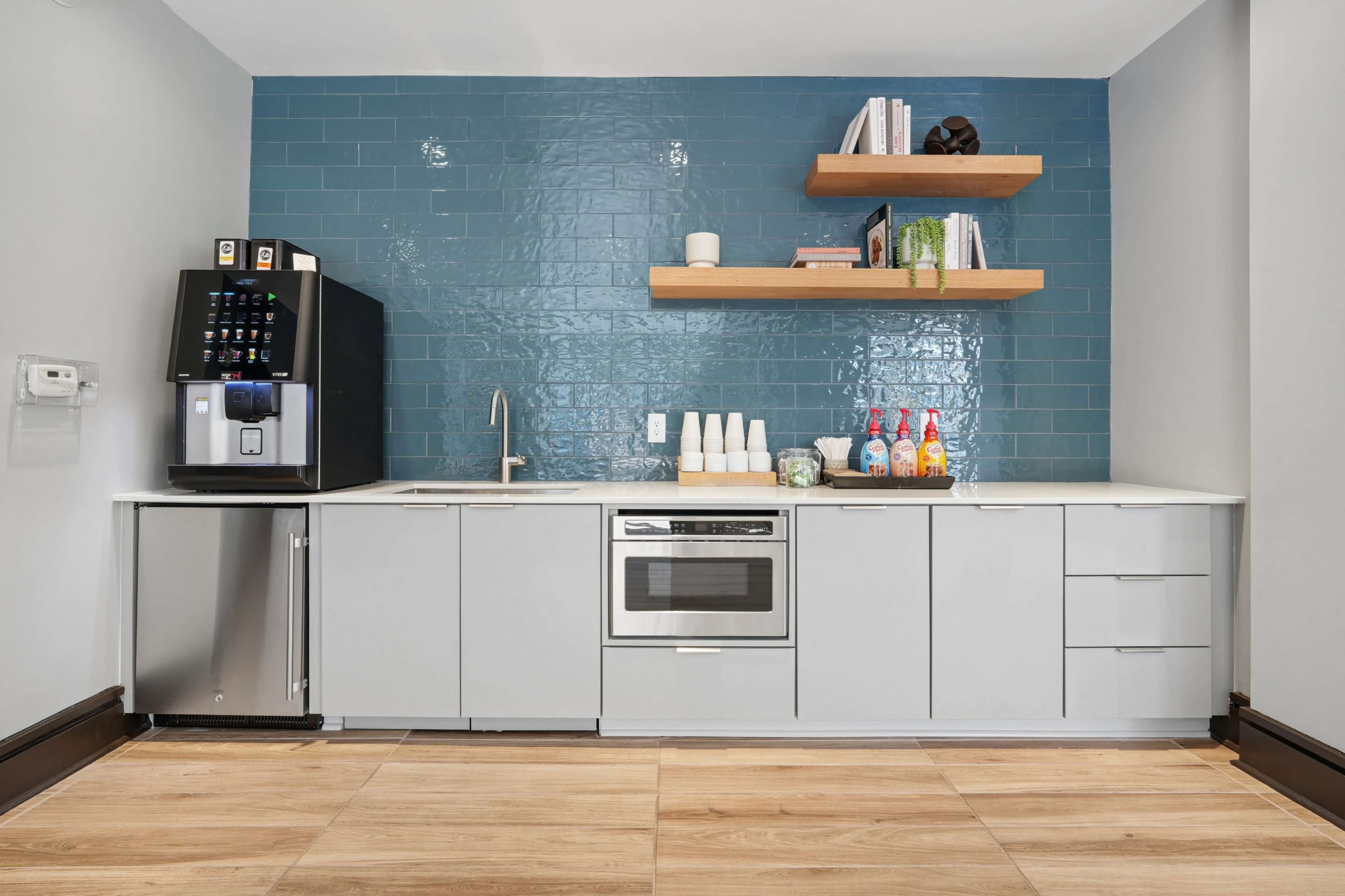 The image displays a modern kitchen space featuring a refrigerator, a sink, and open shelves with decorative items against a blue tiled backsplash.