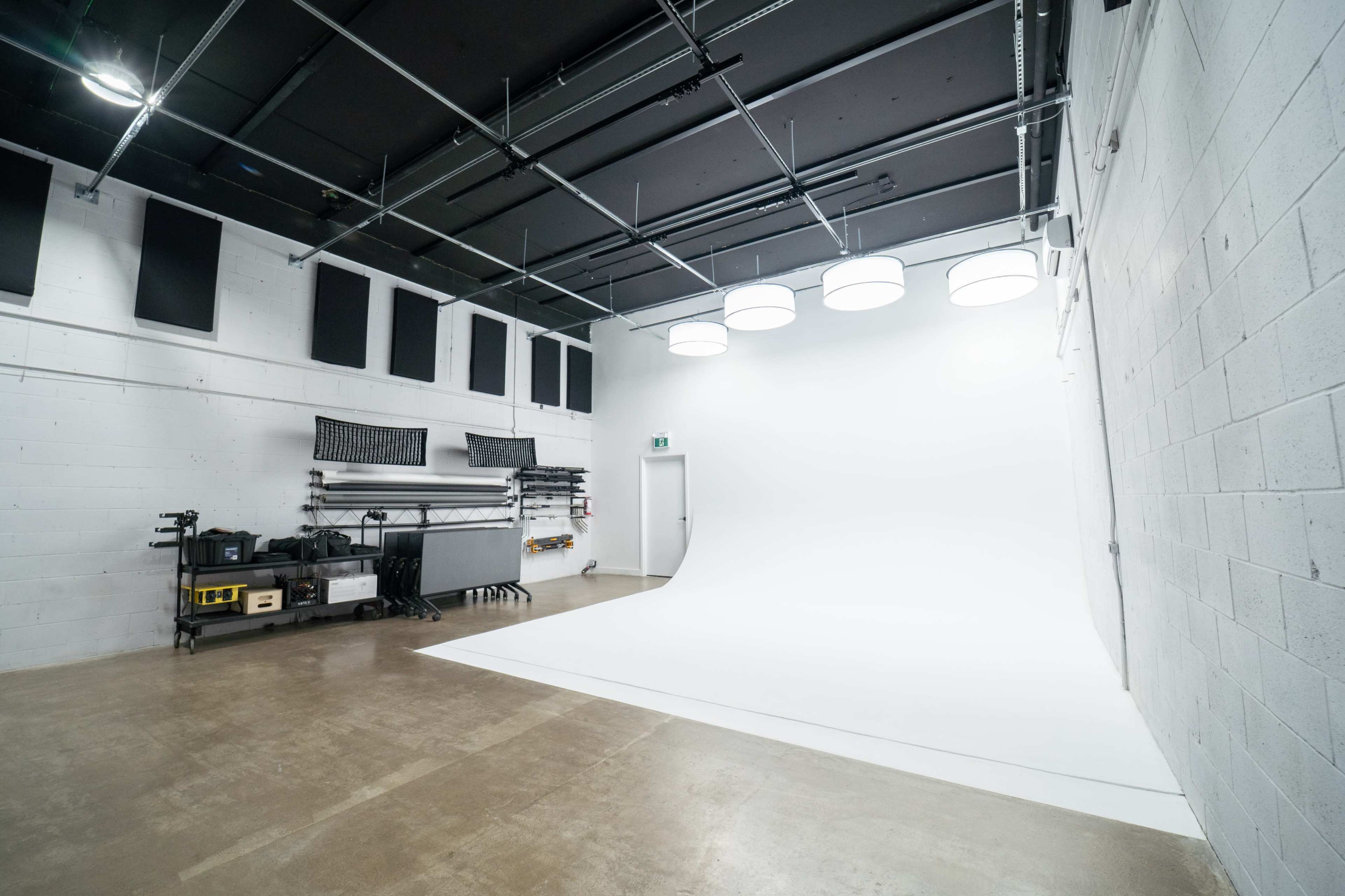 A spacious studio with a white backdrop, equipped with lighting fixtures and storage shelves along one wall.