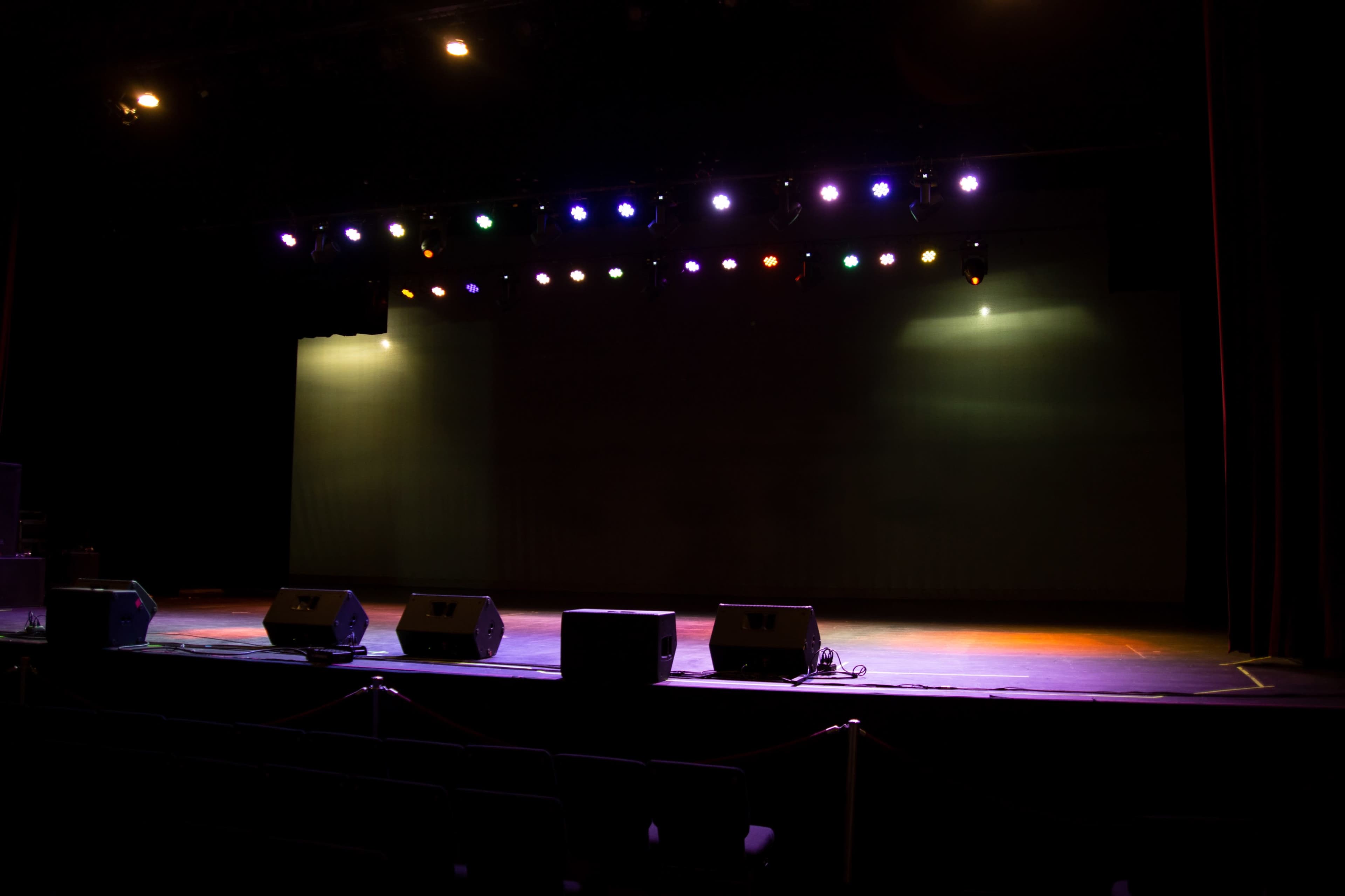 A dimly lit stage with colorful spotlights and sound equipment arranged in front.