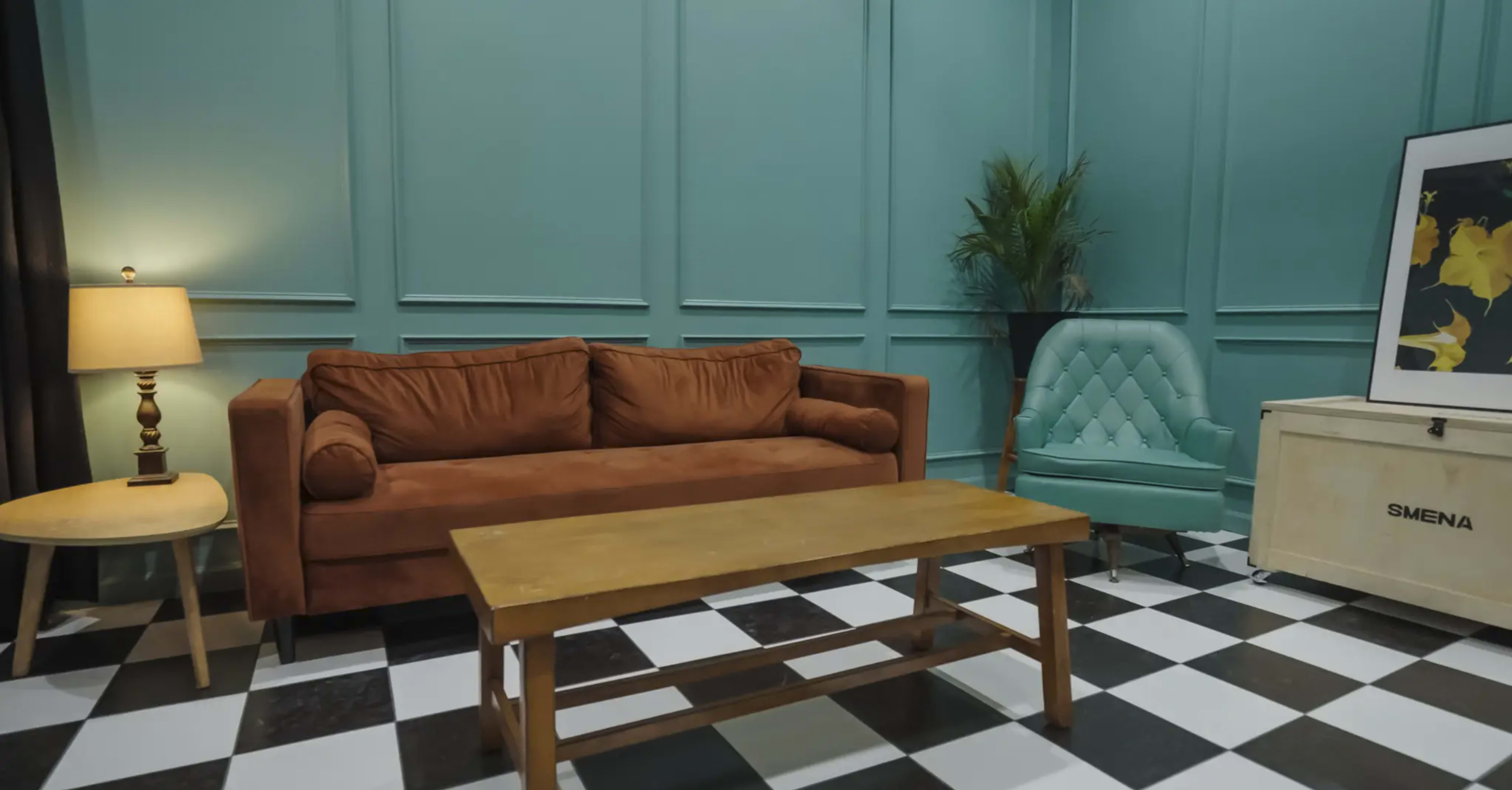The image features a teal-walled room with a brown sofa, a light green armchair, a wooden coffee table, and a lamp on a small side table.