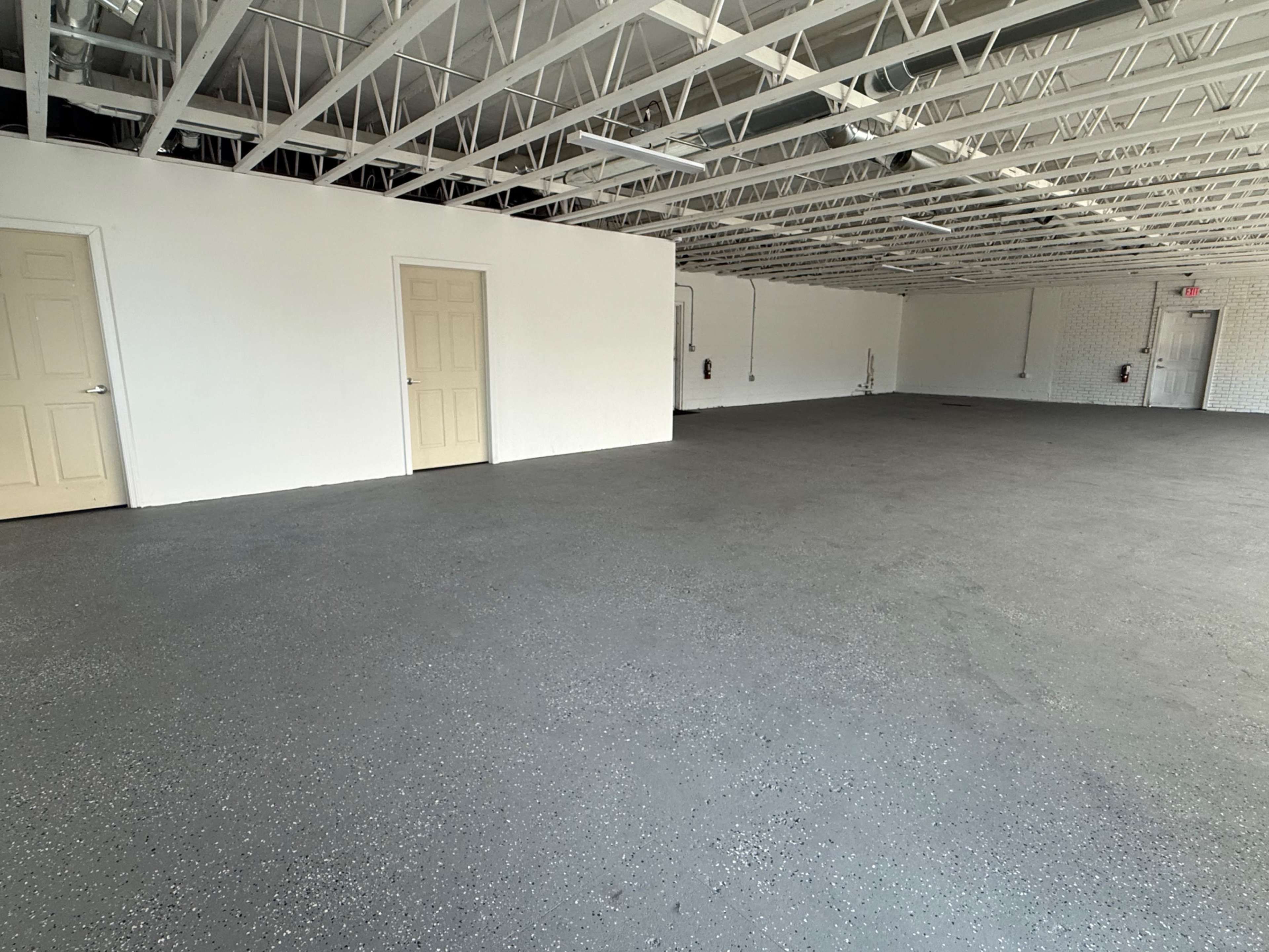 The image shows an empty room with a concrete floor, white walls, and several closed doors along one side.