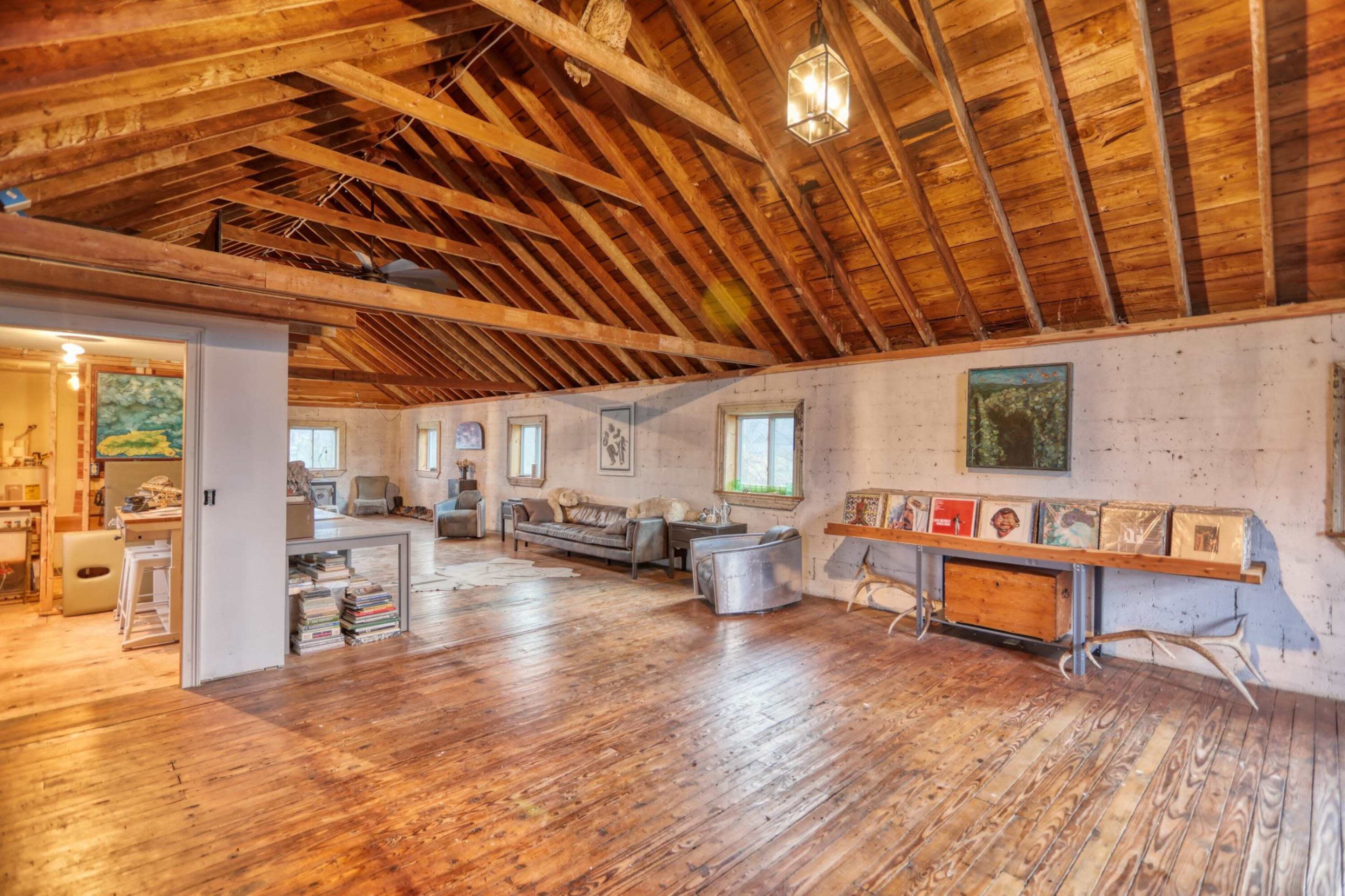 A spacious interior with wooden beams, a polished wooden floor, and a cozy arrangement of furniture, including a sofa and shelves filled with books and art.