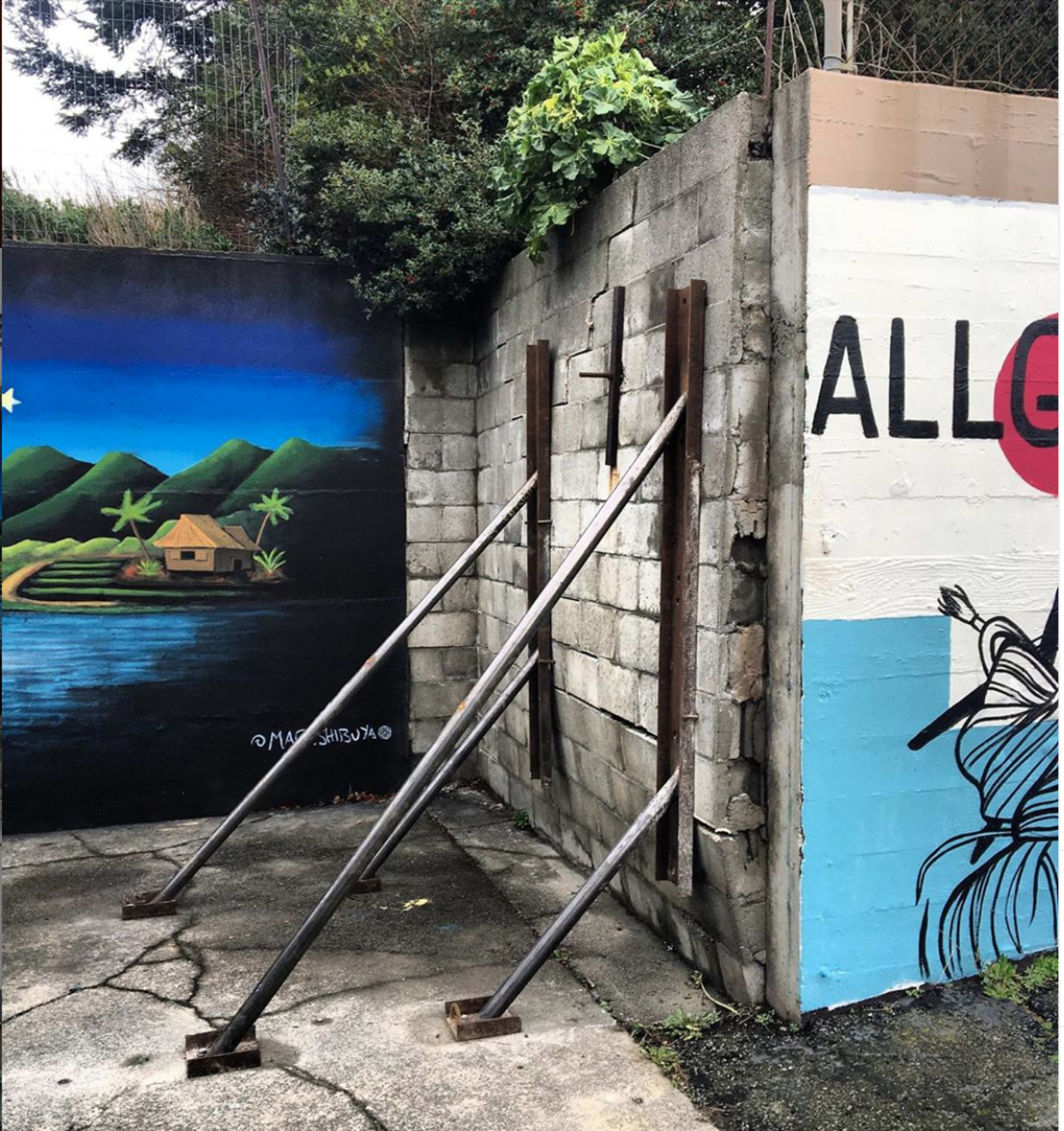 A concrete wall with two metal support beams angled against it, flanked by colorful murals depicting a landscape and vibrant designs.