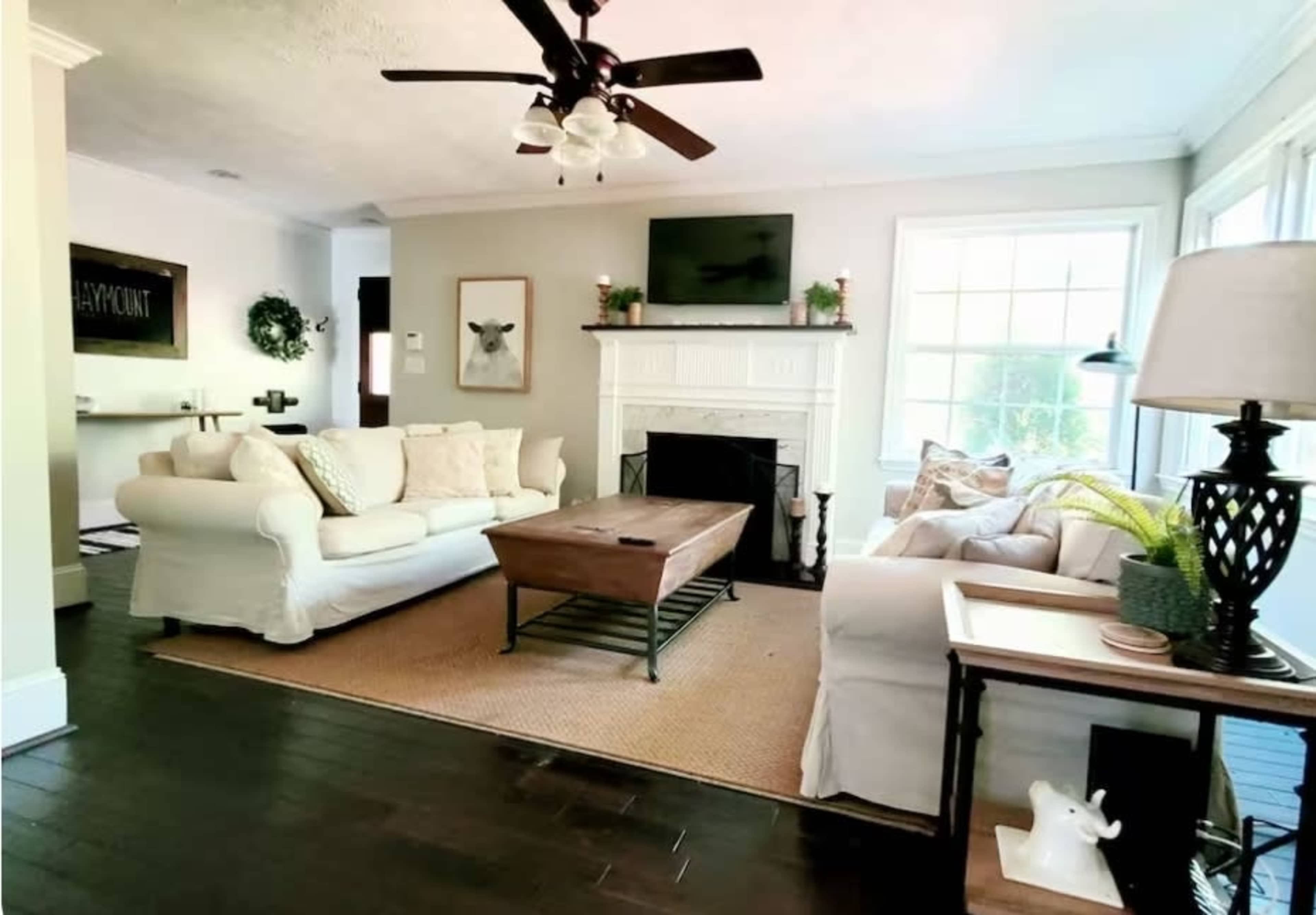 The living room features two sofas, a wooden coffee table, a fireplace with a TV above it, and large windows allowing natural light to fill the space.