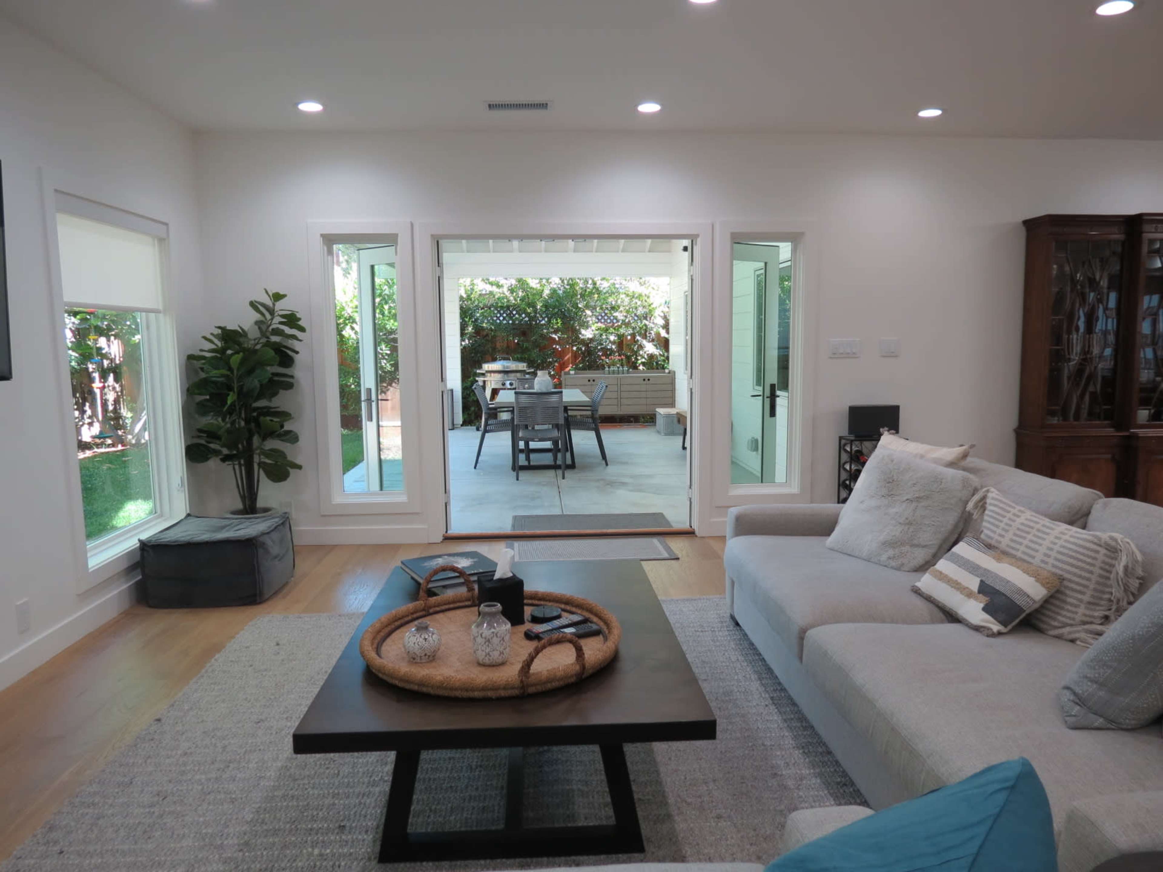 A modern living room features a light-colored sofa, a wooden coffee table with decorative items, and opens to a patio with outdoor seating through glass doors.