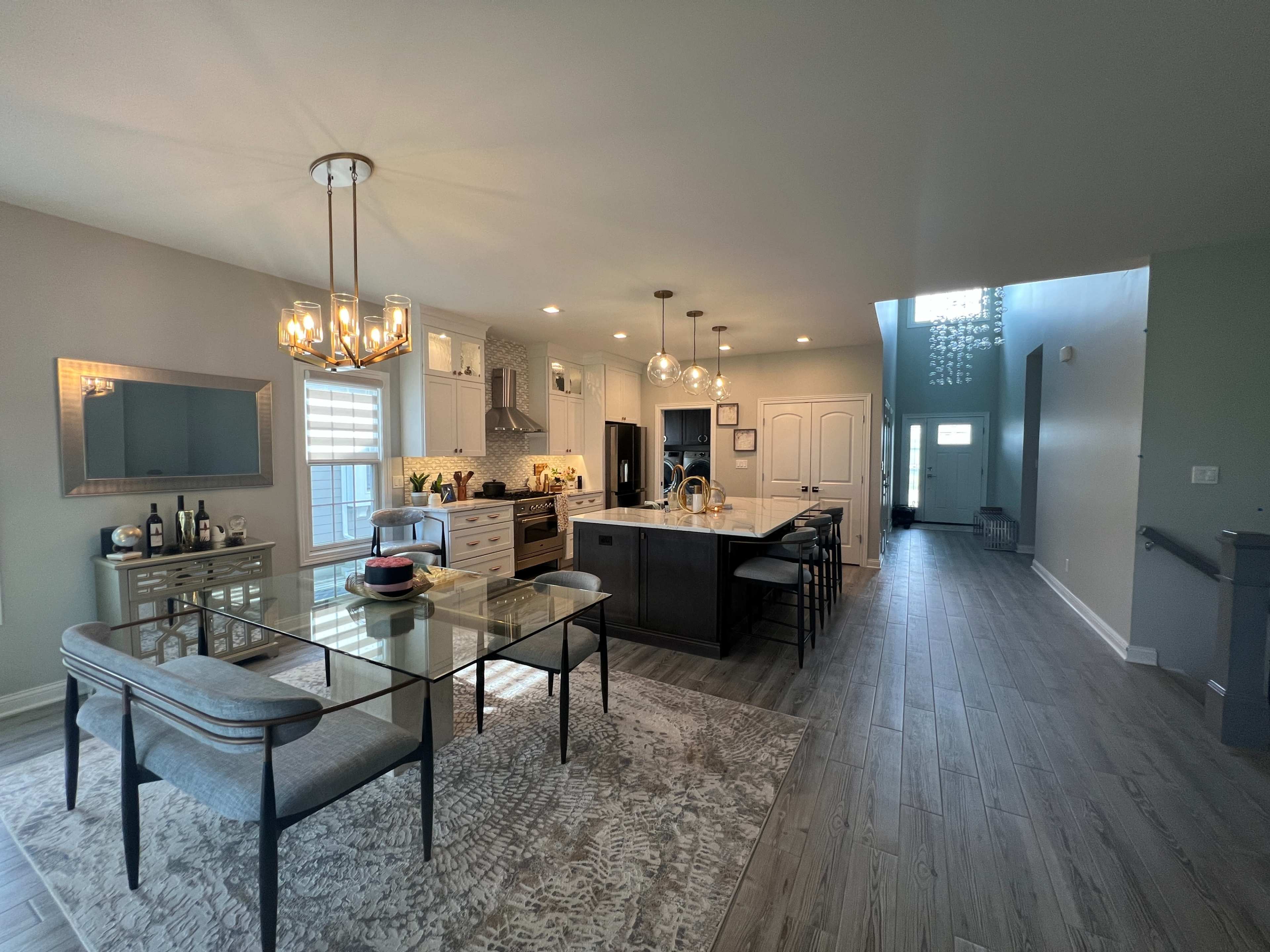 The image shows a modern kitchen and dining area with a glass dining table, gray upholstered chairs, and a large kitchen island.