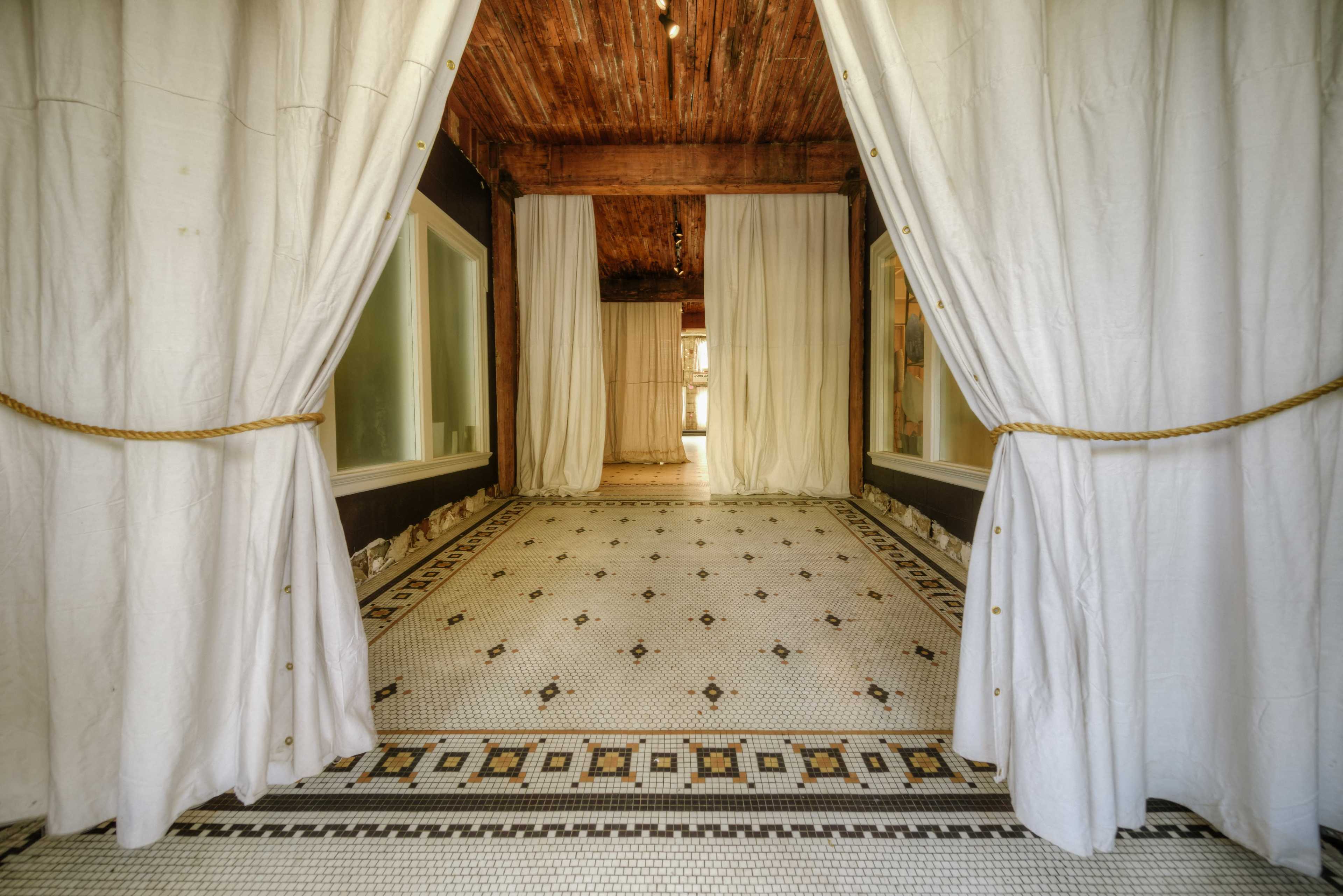 A spacious room with white curtains draped to the sides and a patterned tile floor.