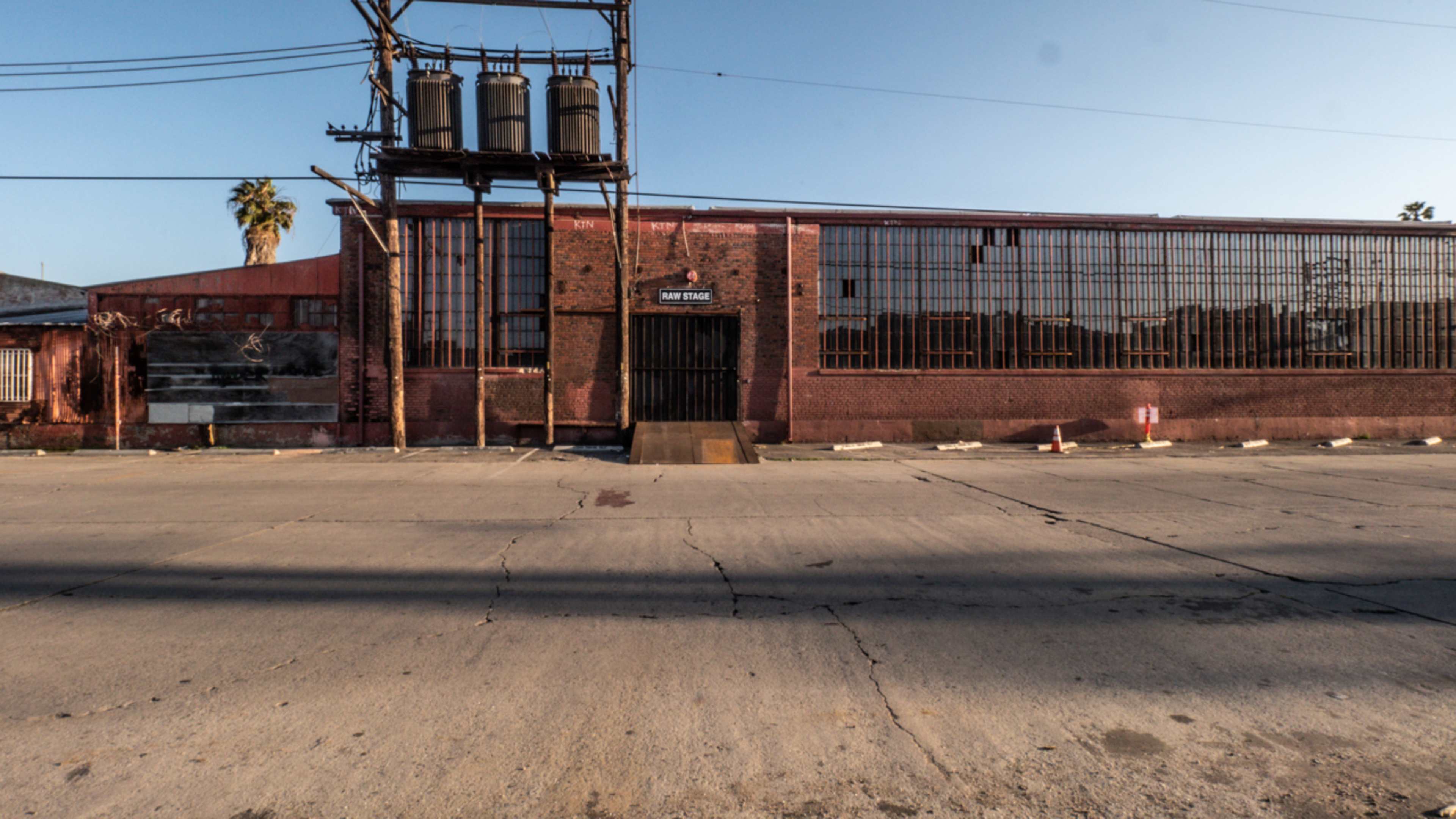 The image shows an empty street in front of a brick warehouse with large windows and utility poles visible.