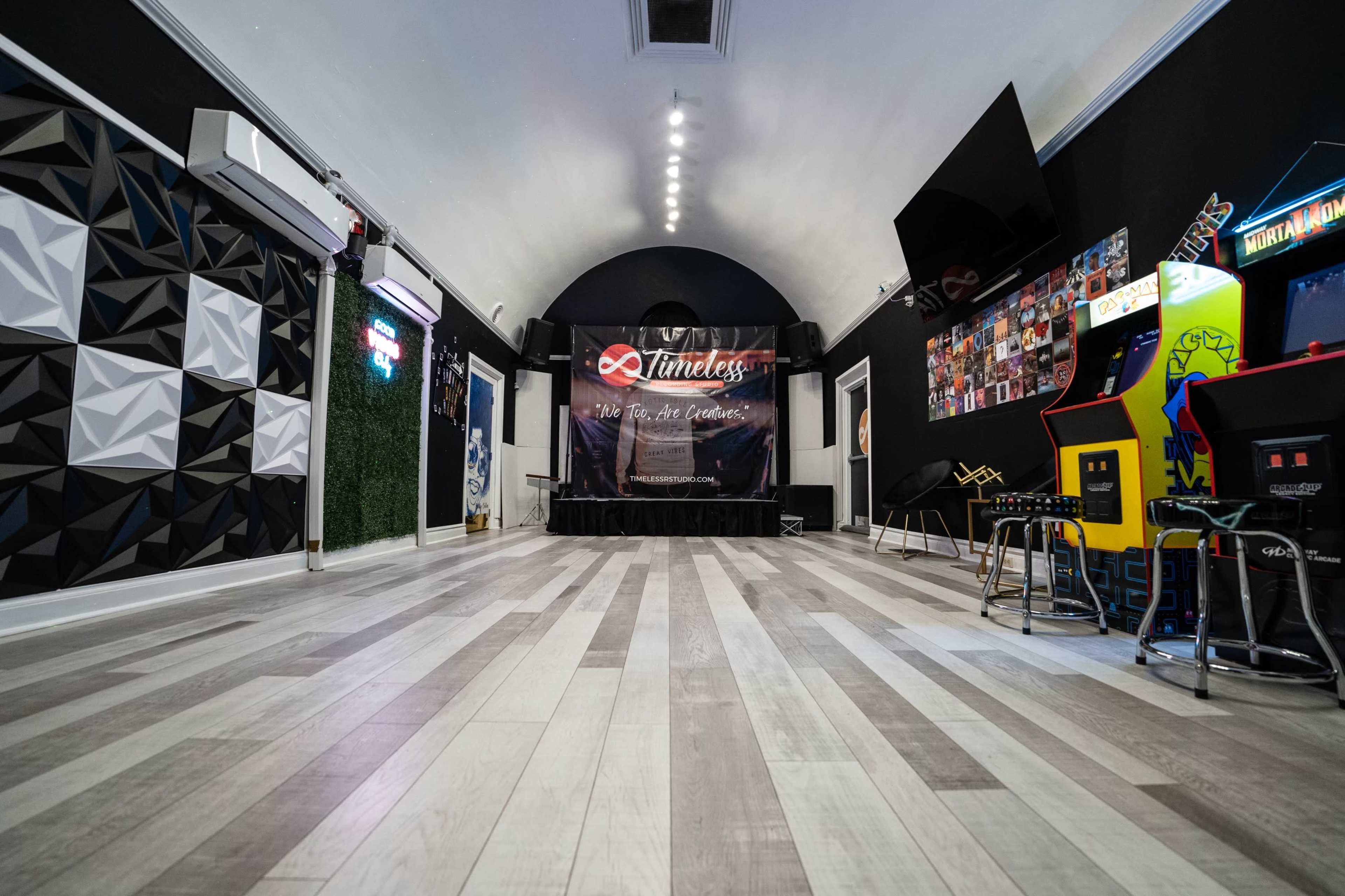 The image shows a modern interior space with a stage, arcade machines, and a sleek floor design.