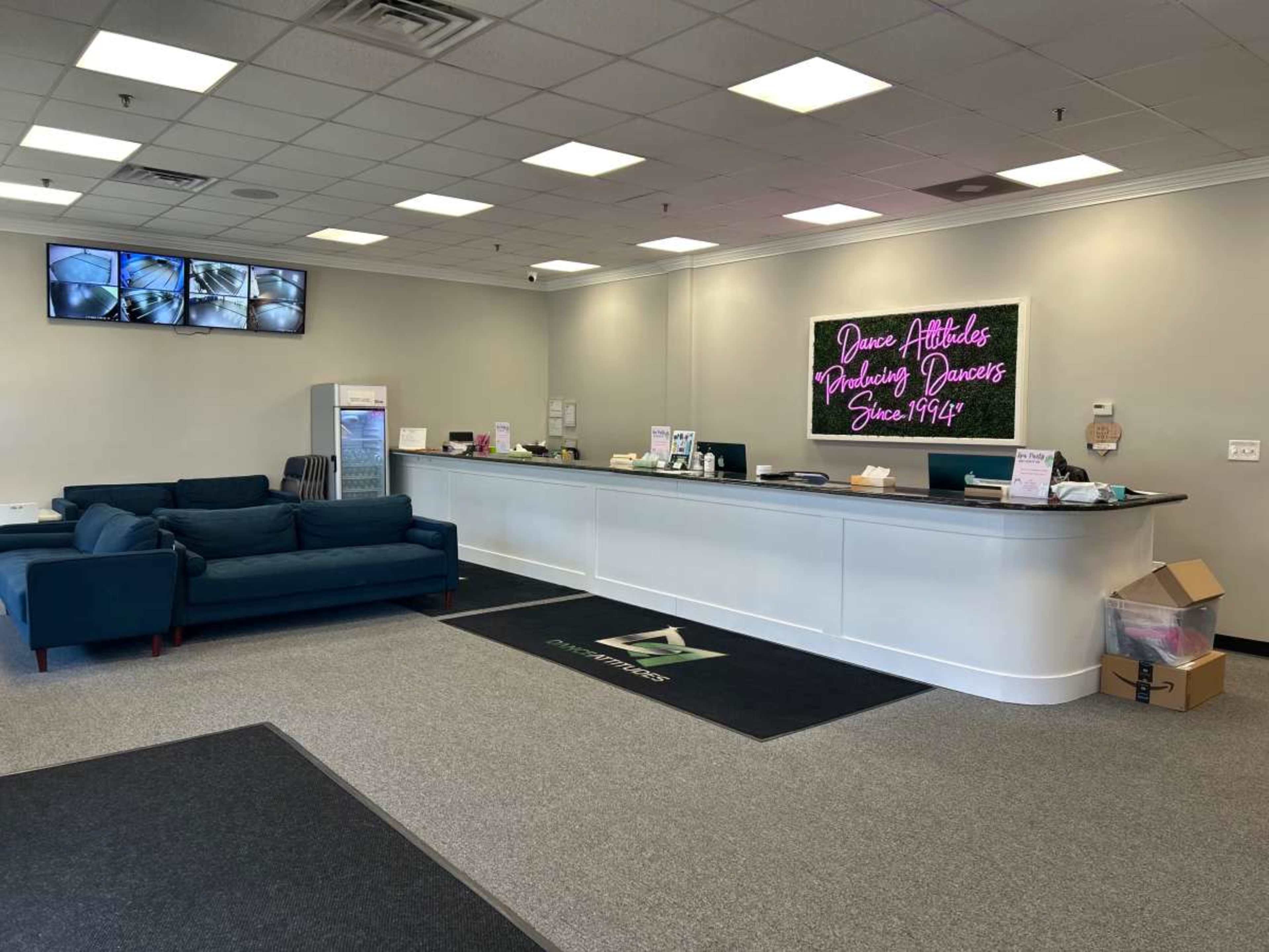 The image shows a spacious reception area with a large counter, a couch, and a neon sign displaying text on the wall.