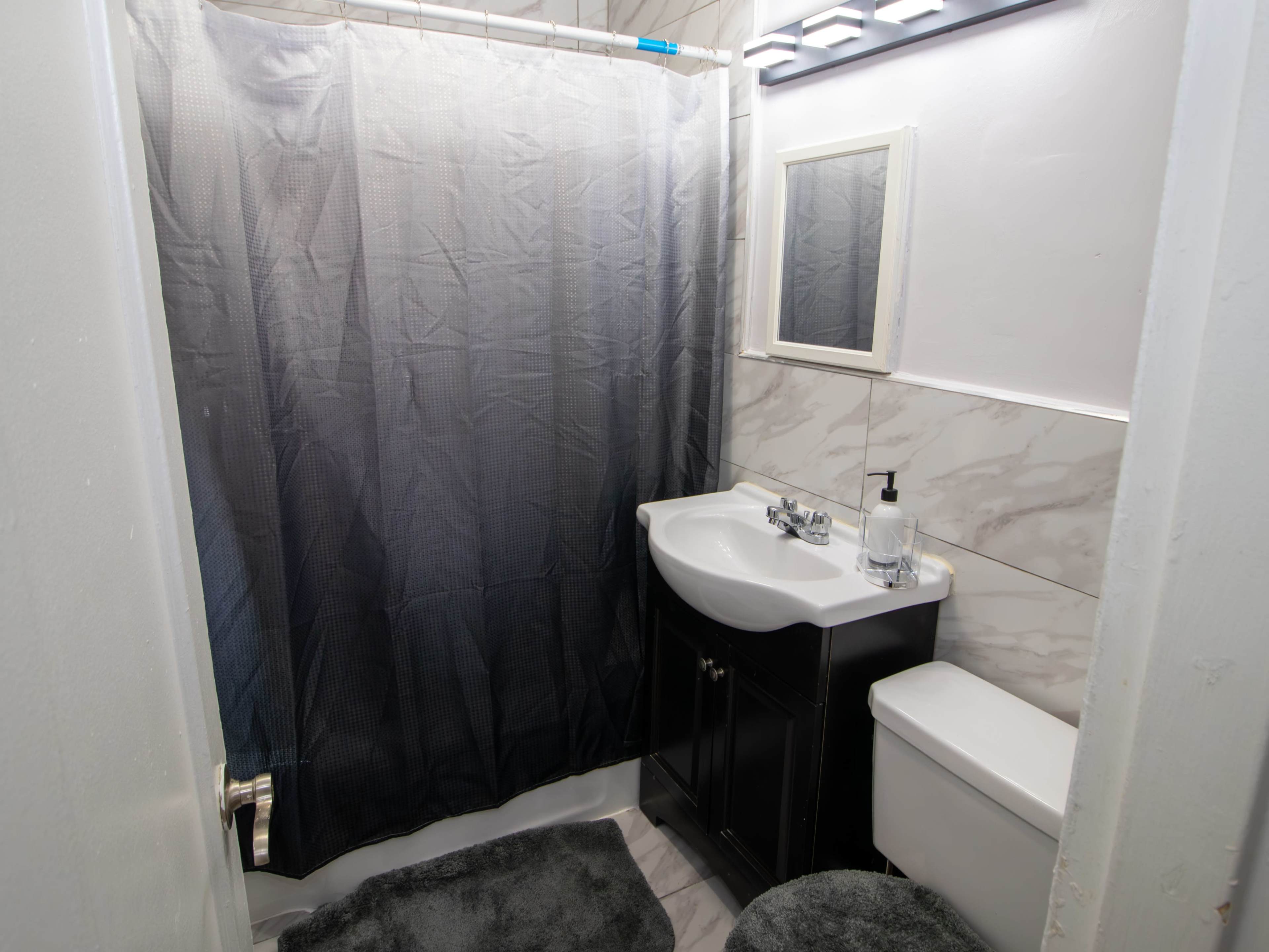 The image shows a bathroom featuring a dark shower curtain, a marble vanity with a sink, a wall mirror, and a toilet.