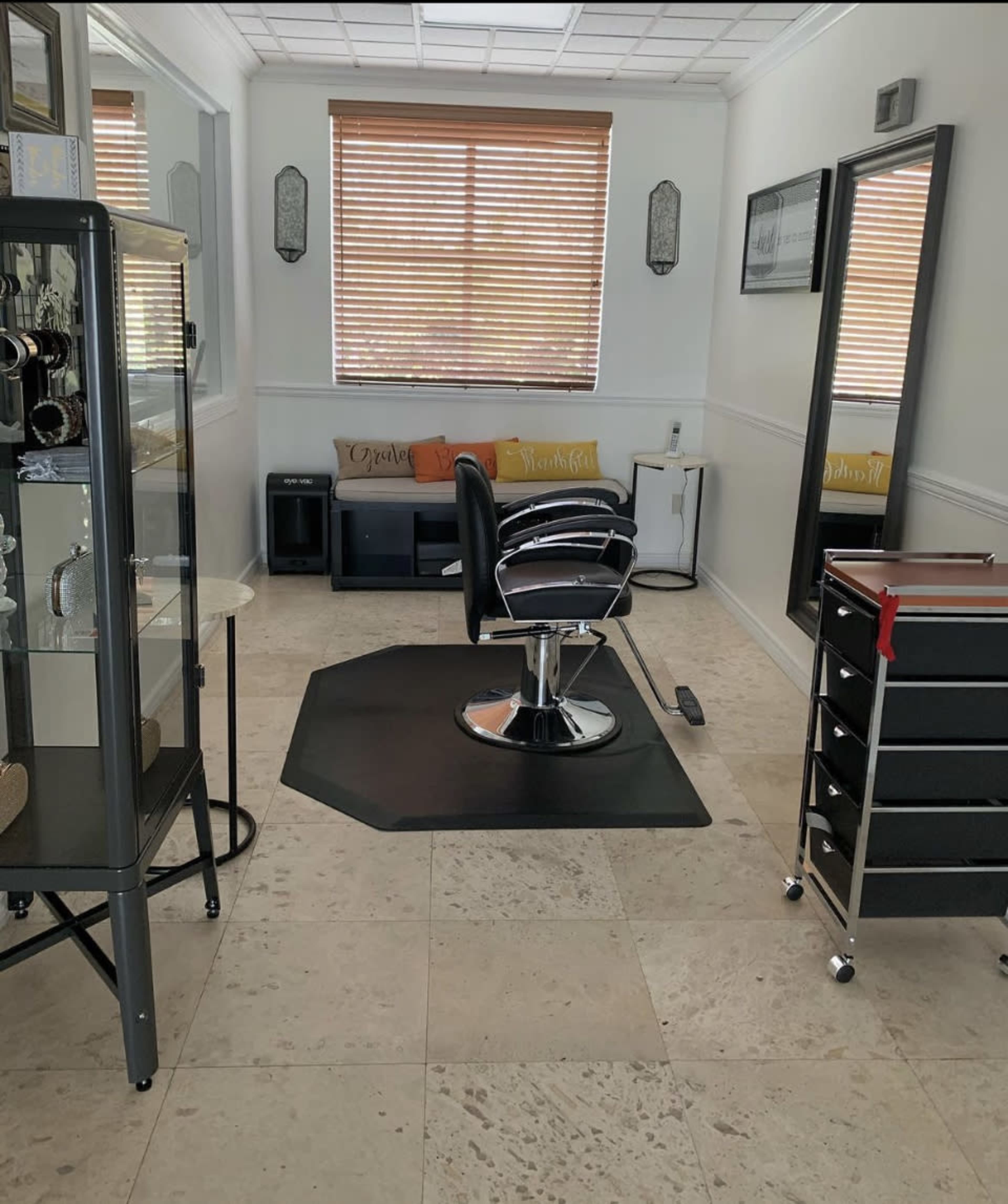 A well-lit hair salon with a styling chair in the center, surrounded by mirrors, storage carts, and a display cabinet.