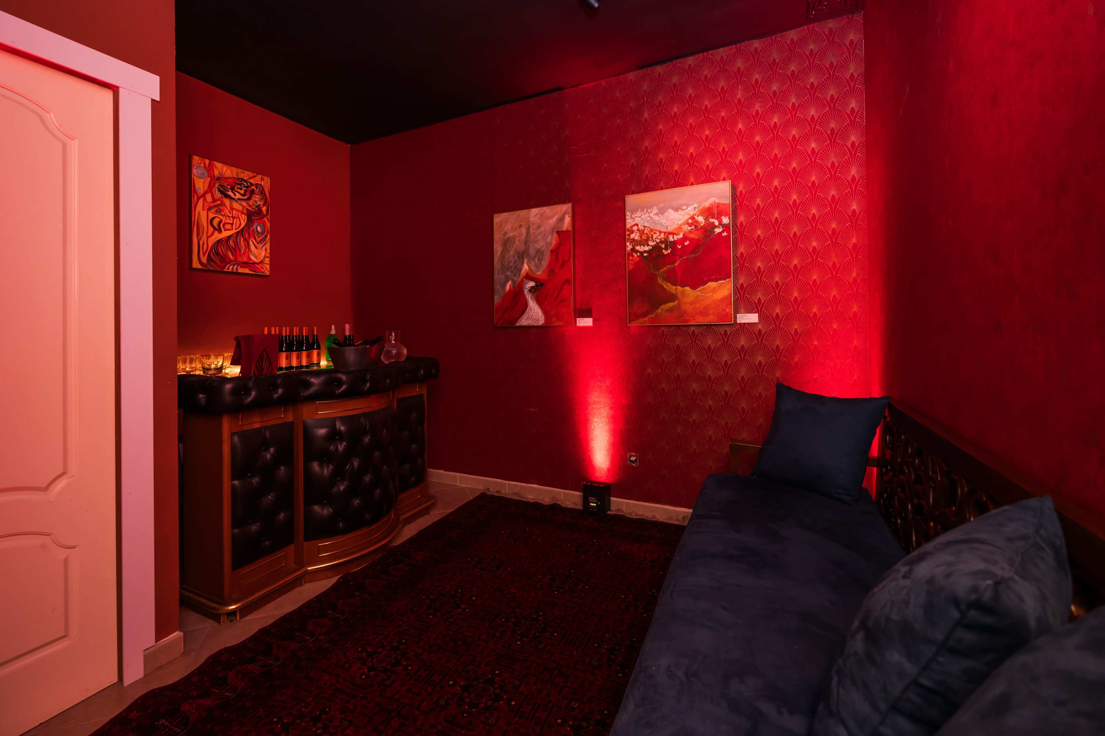 The image shows a cozy room with red walls, featuring a dark sofa and art pieces on the wall, illuminated by soft lighting.