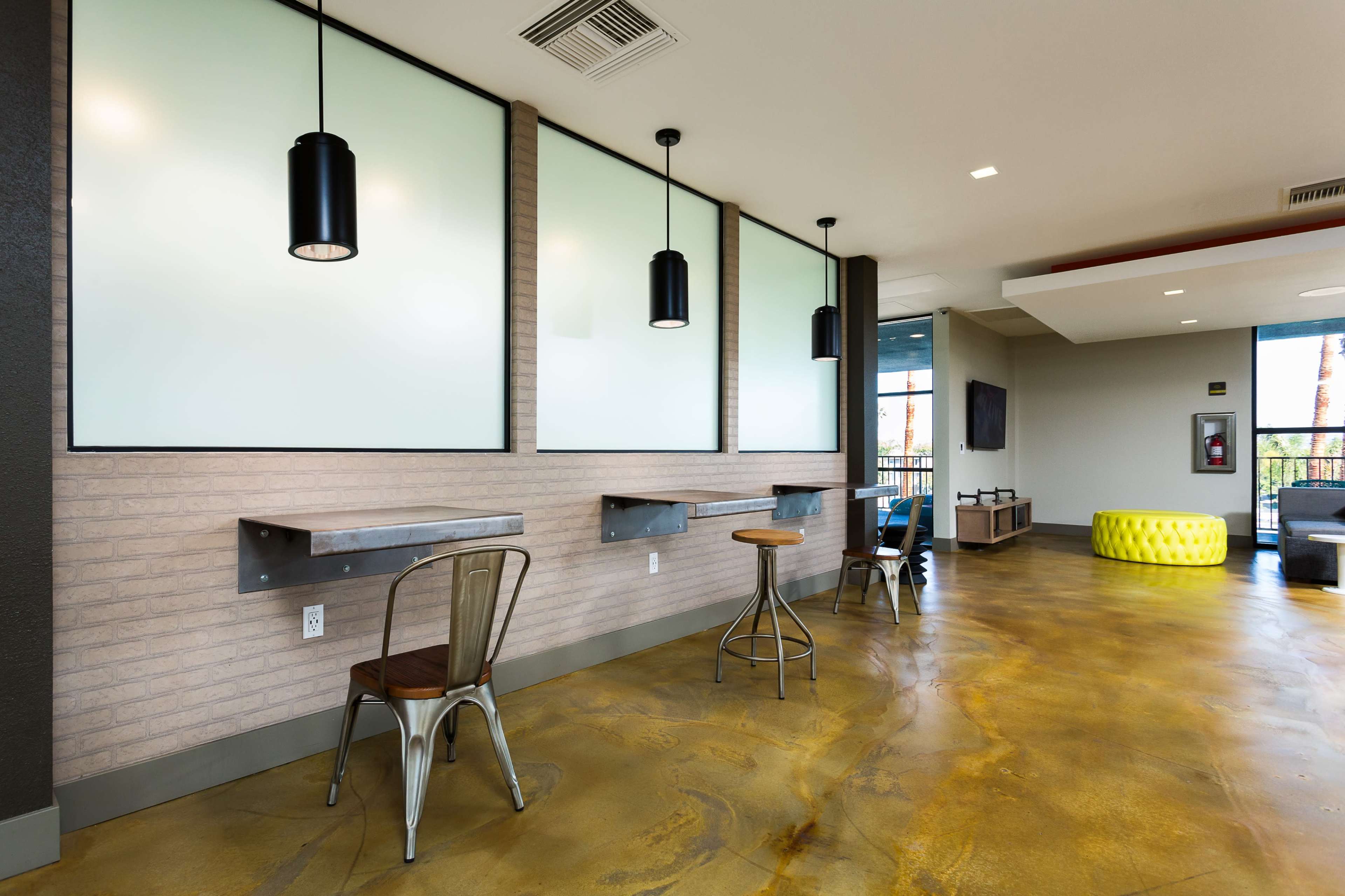 A modern interior space with industrial-style furniture, featuring two workstations, pendant lights, and a yellow seating area.