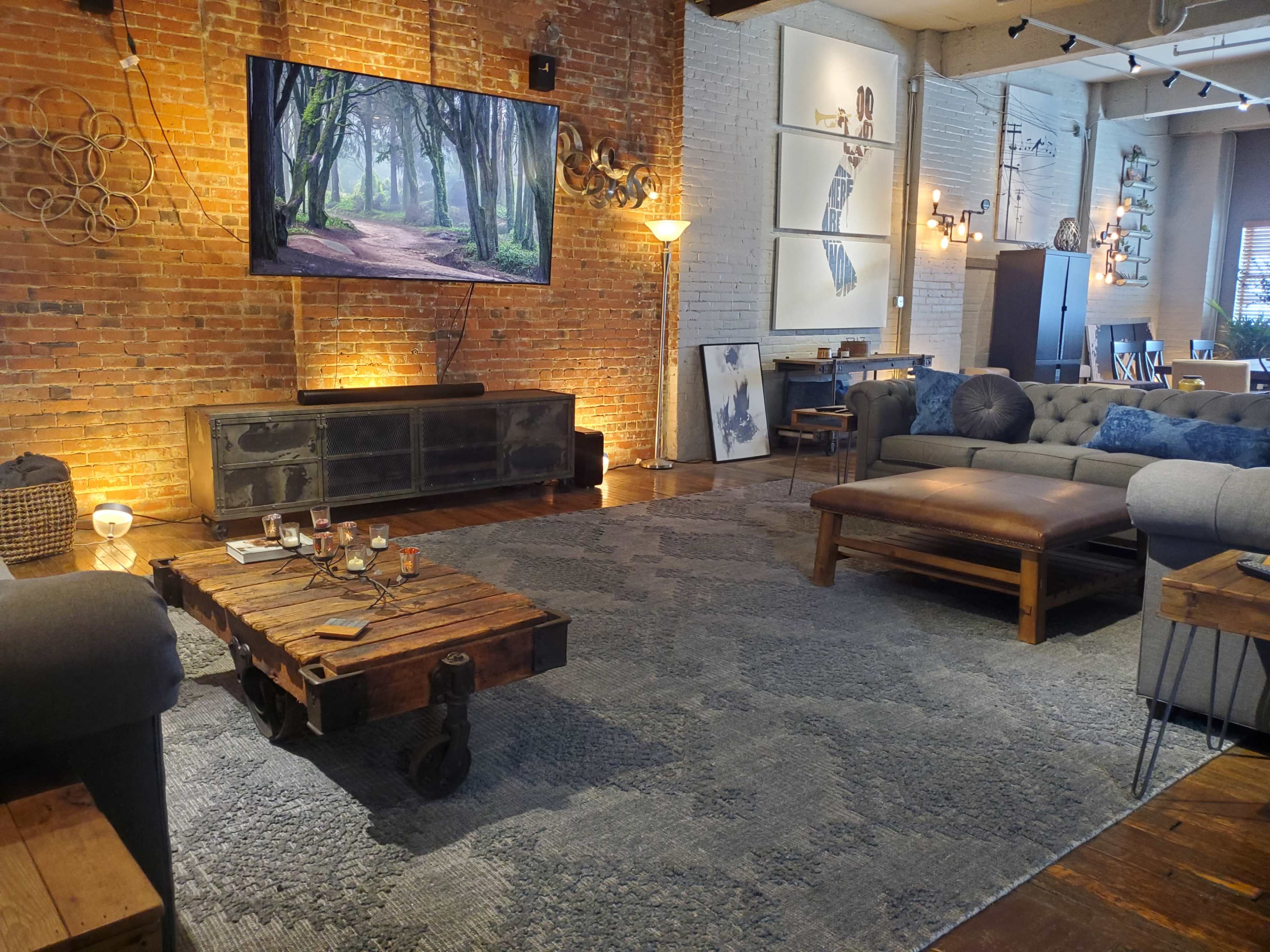 The living room features a large television mounted on a brick wall, with a wooden coffee table on a patterned rug and comfortable seating arranged around the space.