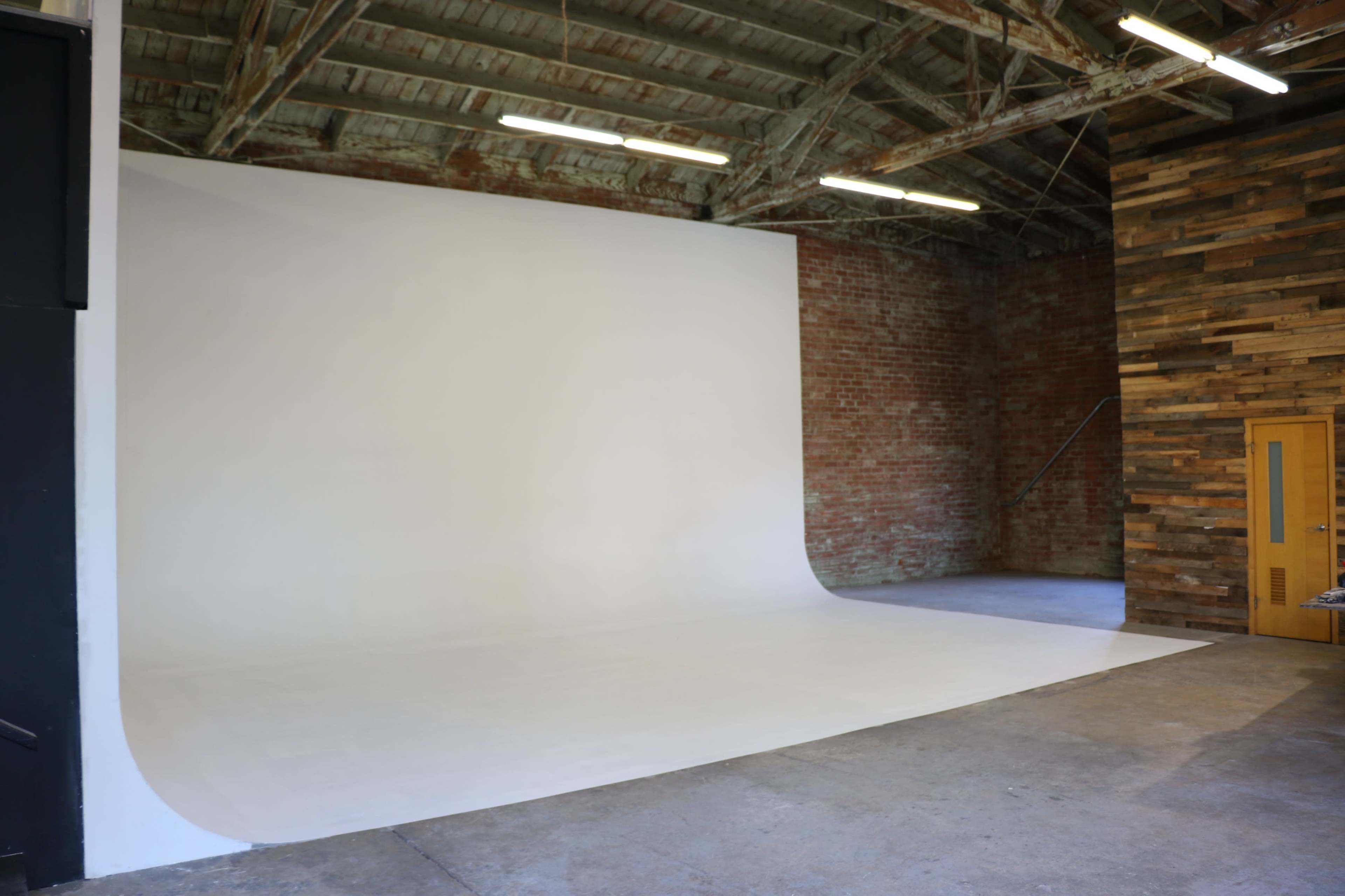 The image shows a spacious studio with a white seamless backdrop, exposed brick walls, and wooden paneling.