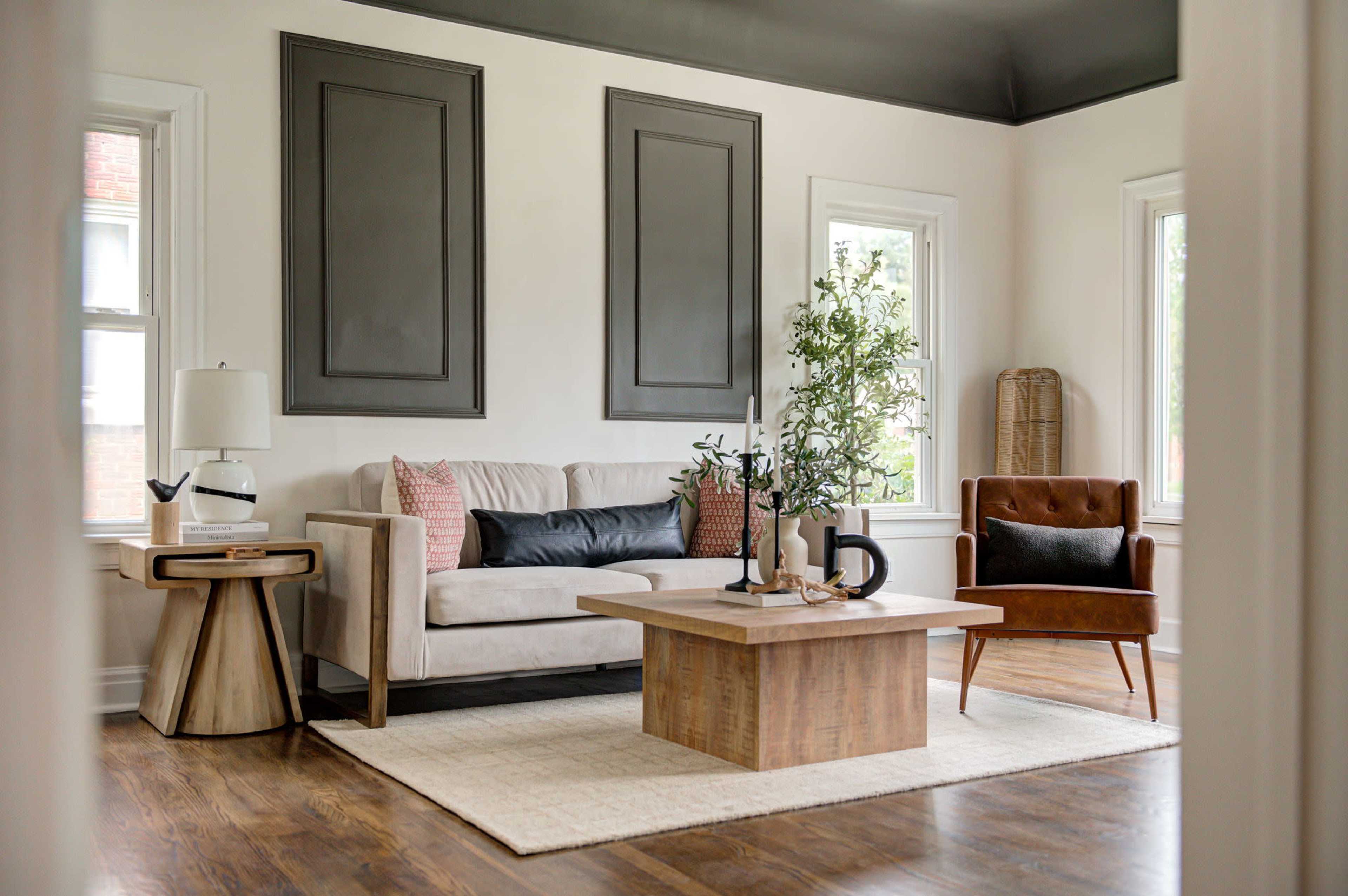 The image shows a modern living room with a light-colored sofa, a wooden coffee table, and an accent chair, complemented by natural light from nearby windows.