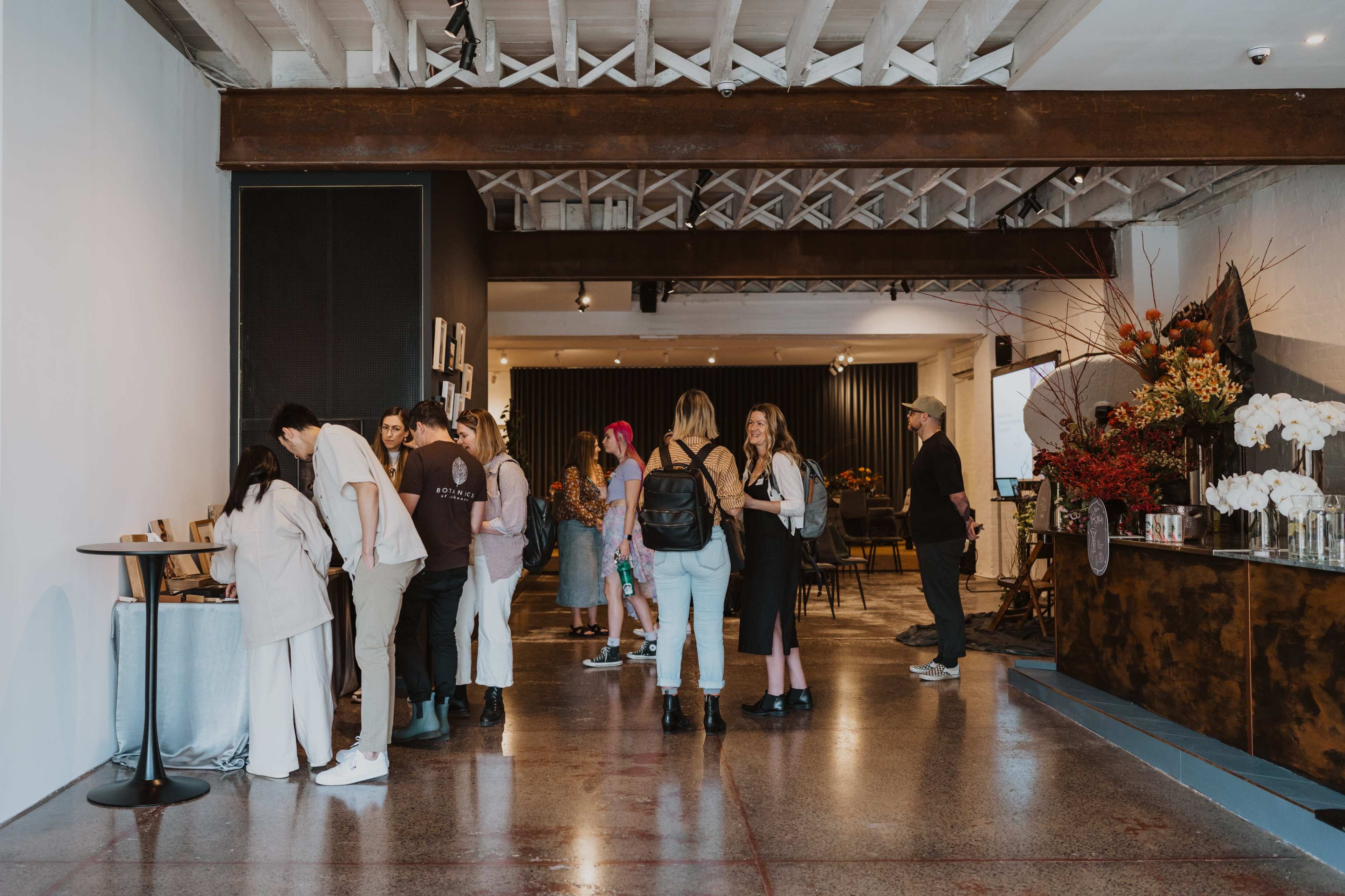 A group of people gathers in a spacious, modern interior, with some engaged in conversation near a service table.
