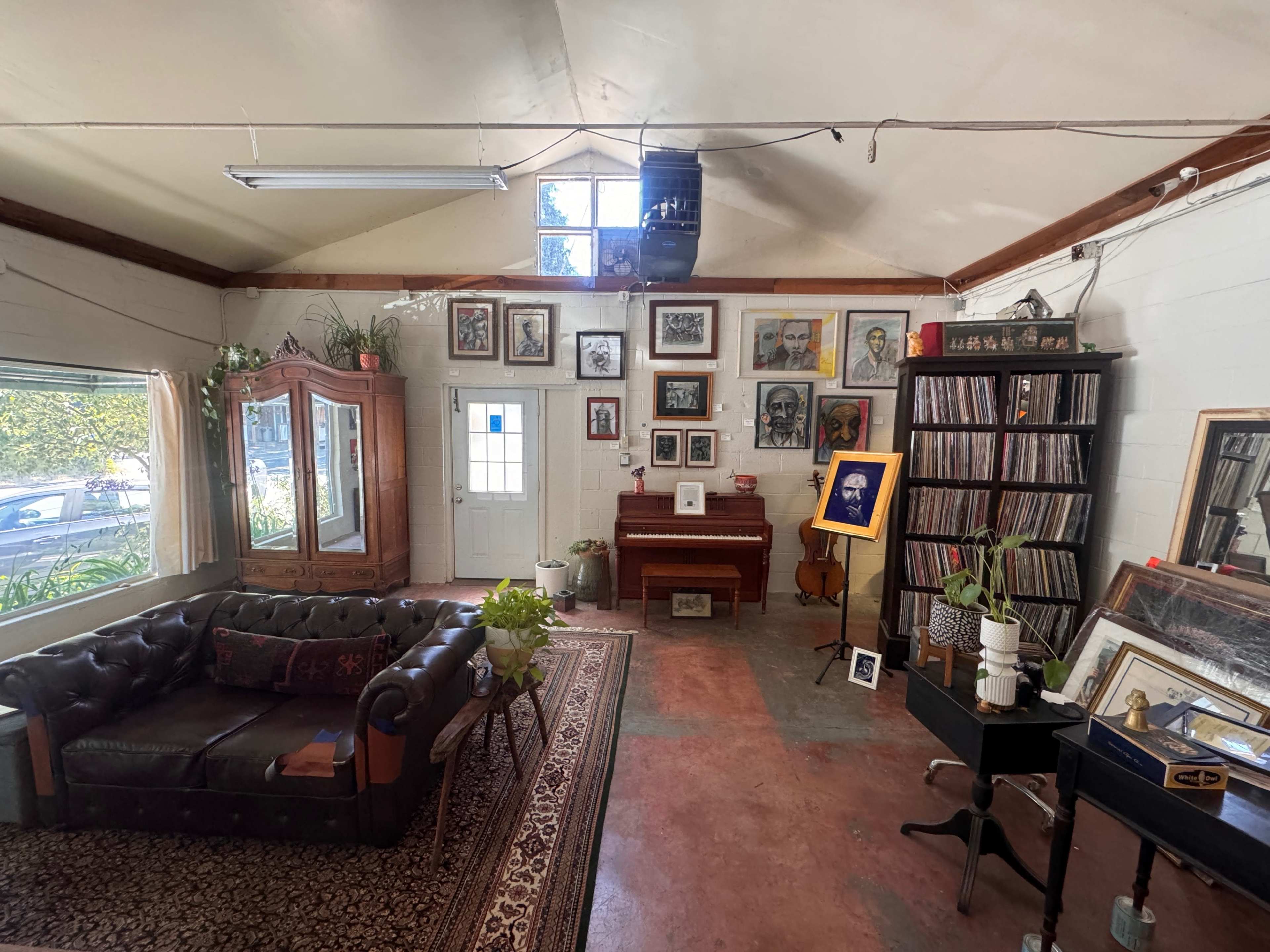 A cozy room featuring a leather couch, a piano, various framed artworks on the walls, and a record collection in a cabinet.