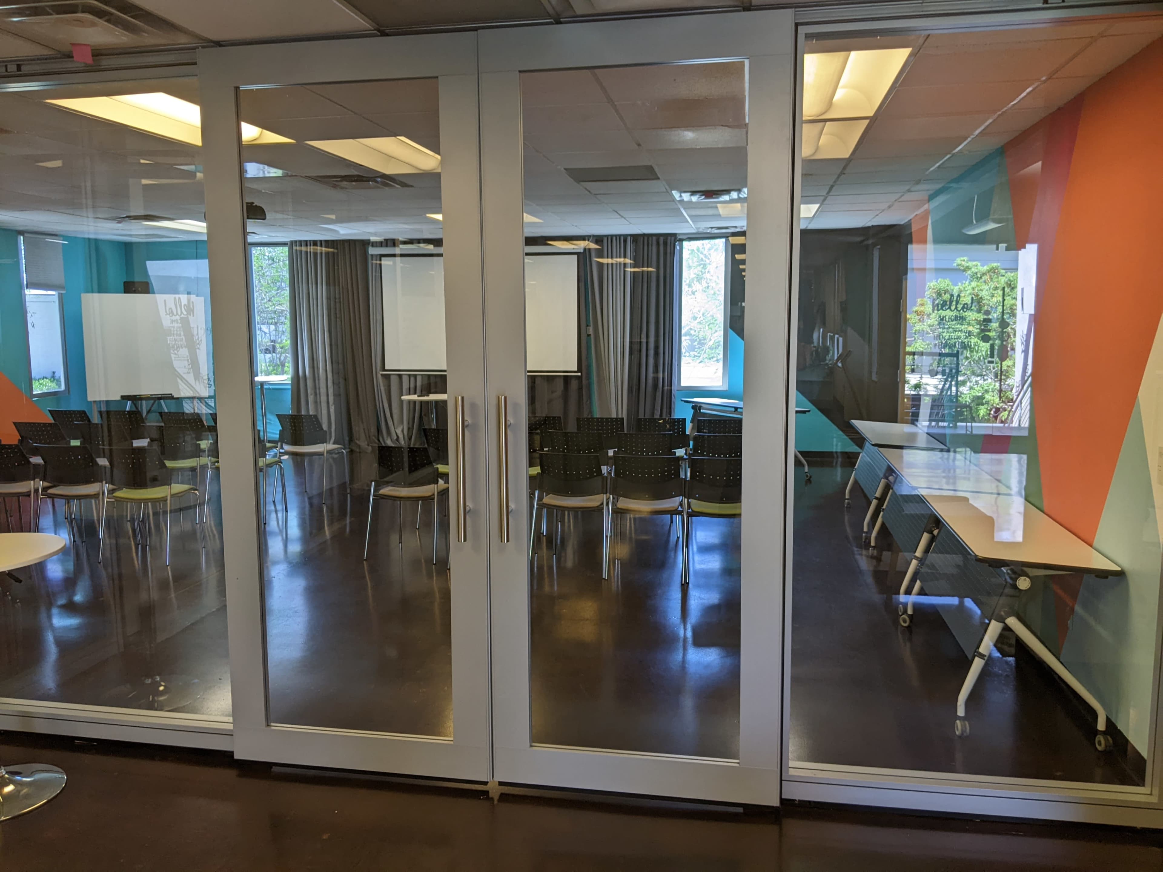 A modern conference room with glass doors, featuring rows of black chairs and tables arranged for a meeting.