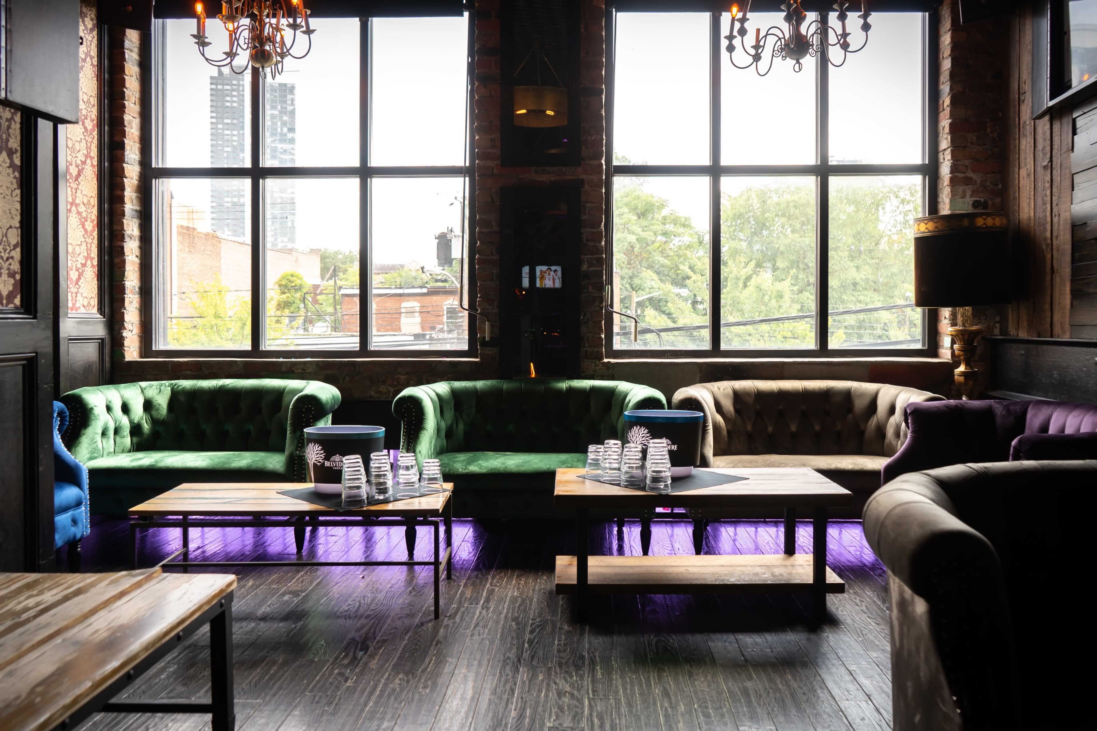 A lounge area with green and purple couches, wooden tables, and large windows allowing natural light to enter.