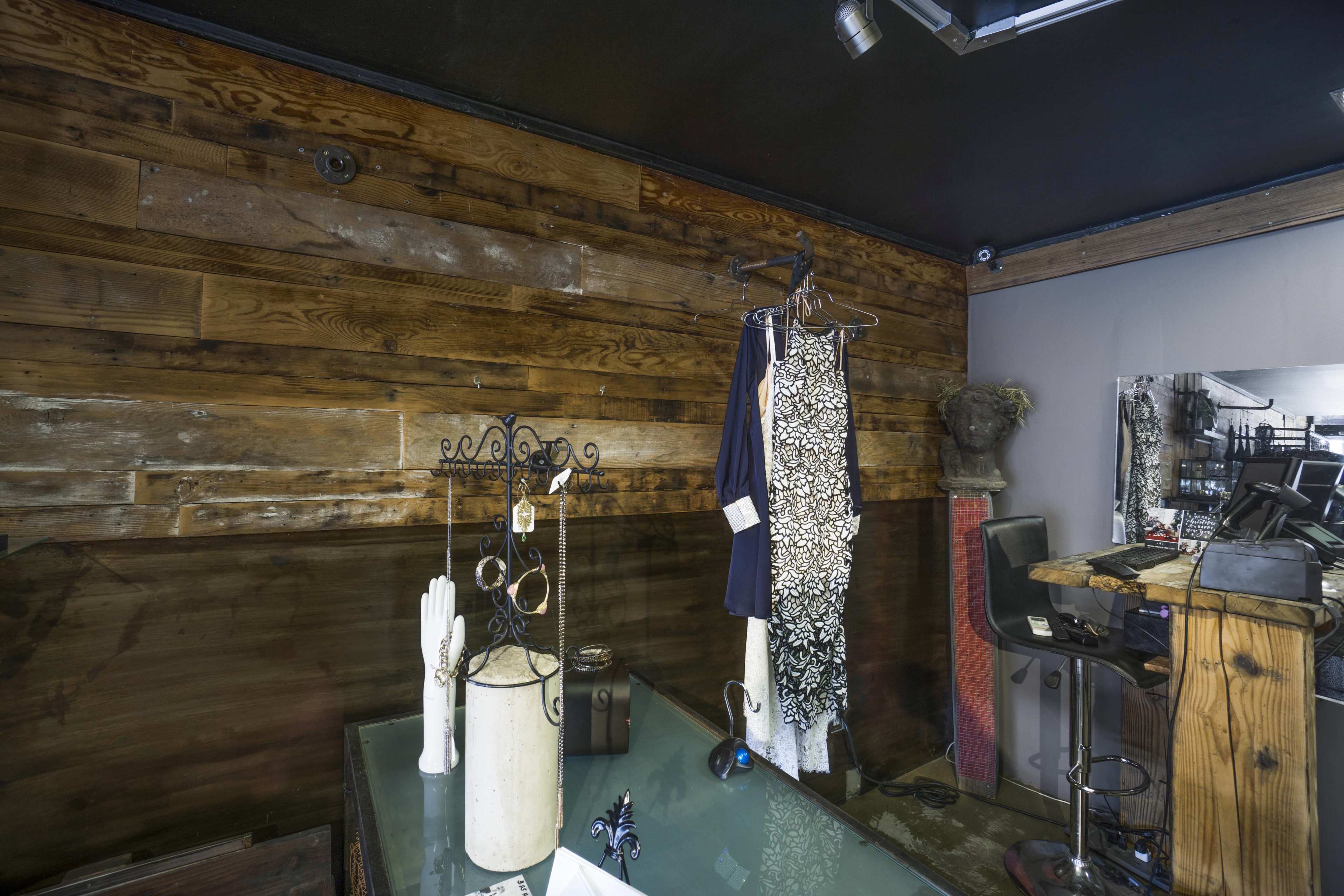 A boutique interior with wooden walls, a clothing rack displaying a dress, and a decorative display stand on a glass table.