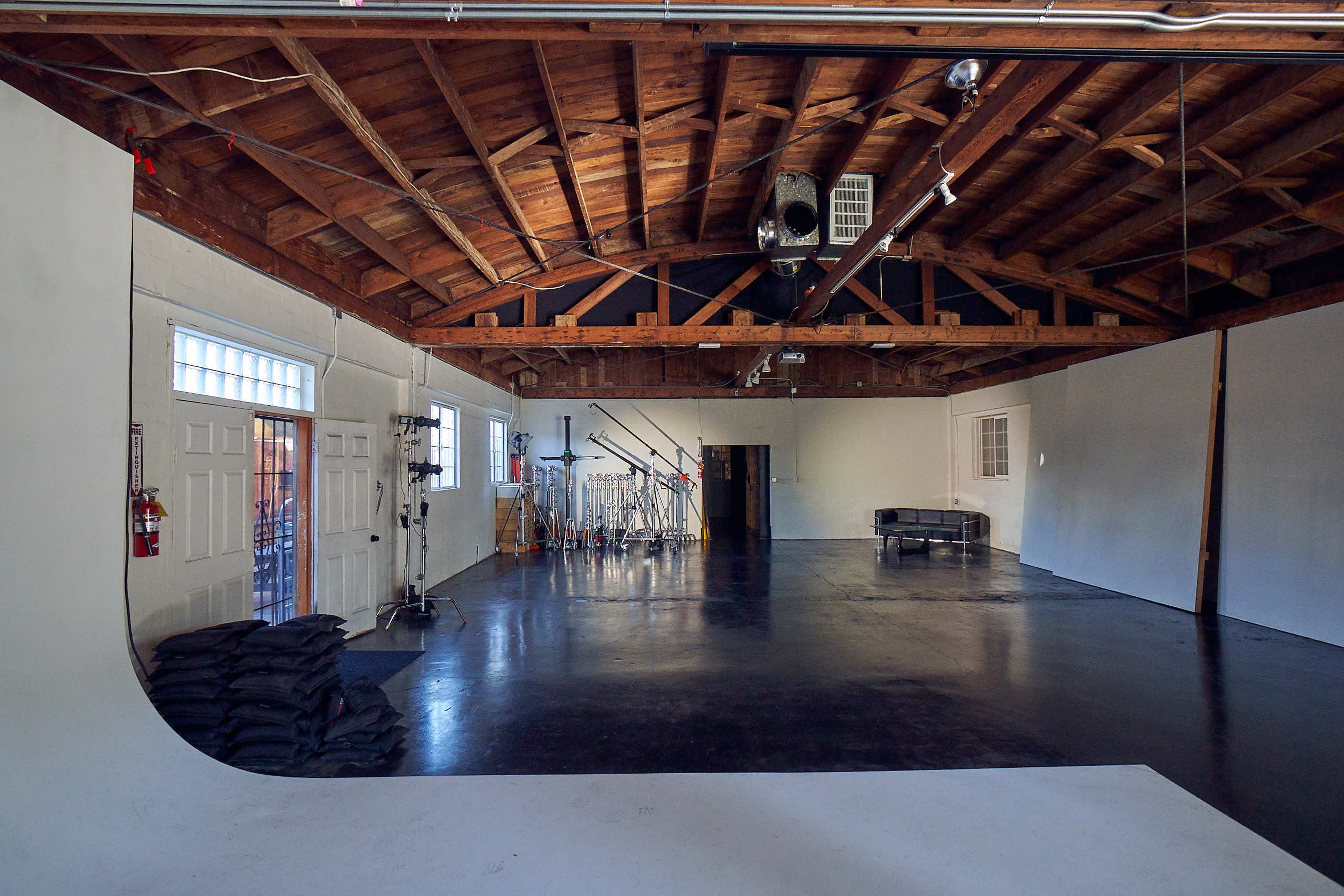The image shows a spacious studio with a high wooden ceiling, equipped with a backdrop and various photography equipment arranged in the background.
