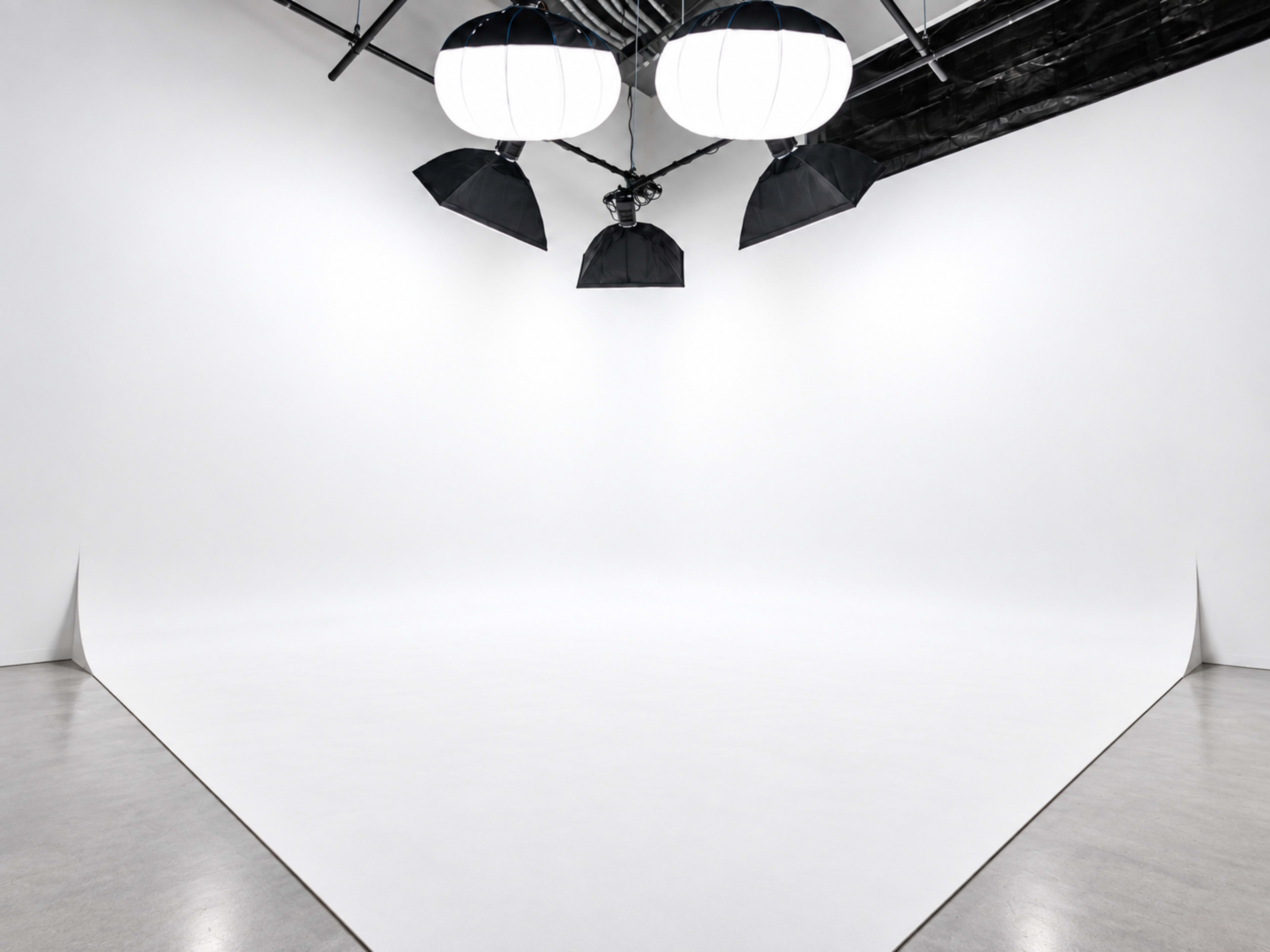 The image shows a spacious photography studio with a seamless white backdrop and large overhead lighting equipment.