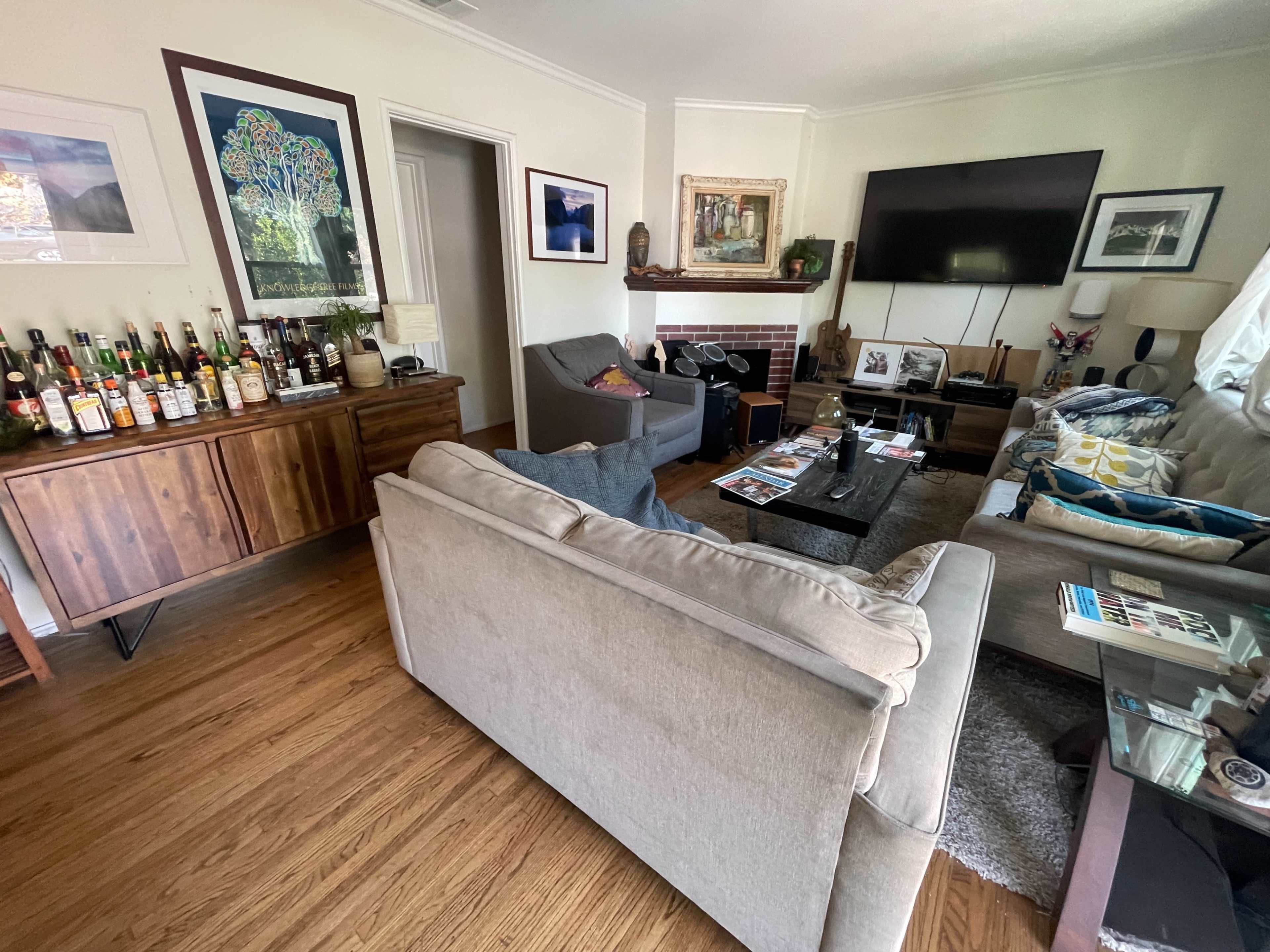 A cozy living room with a sofa, an armchair, a coffee table, and a wooden sideboard displaying various bottles.