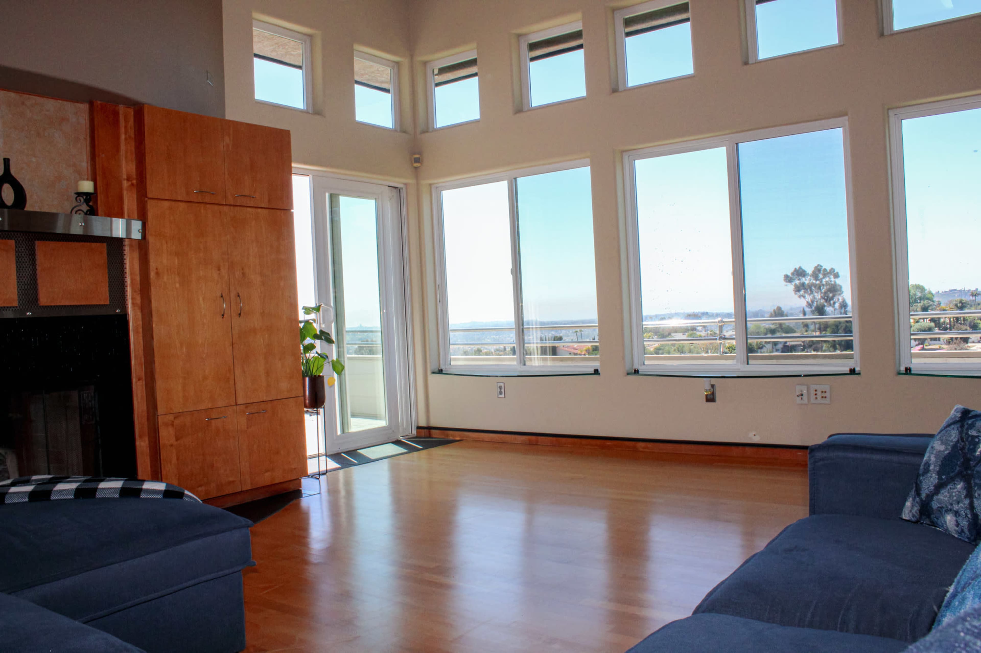 A spacious living room with large windows overlooking a distant view, featuring a fireplace and wooden cabinetry.