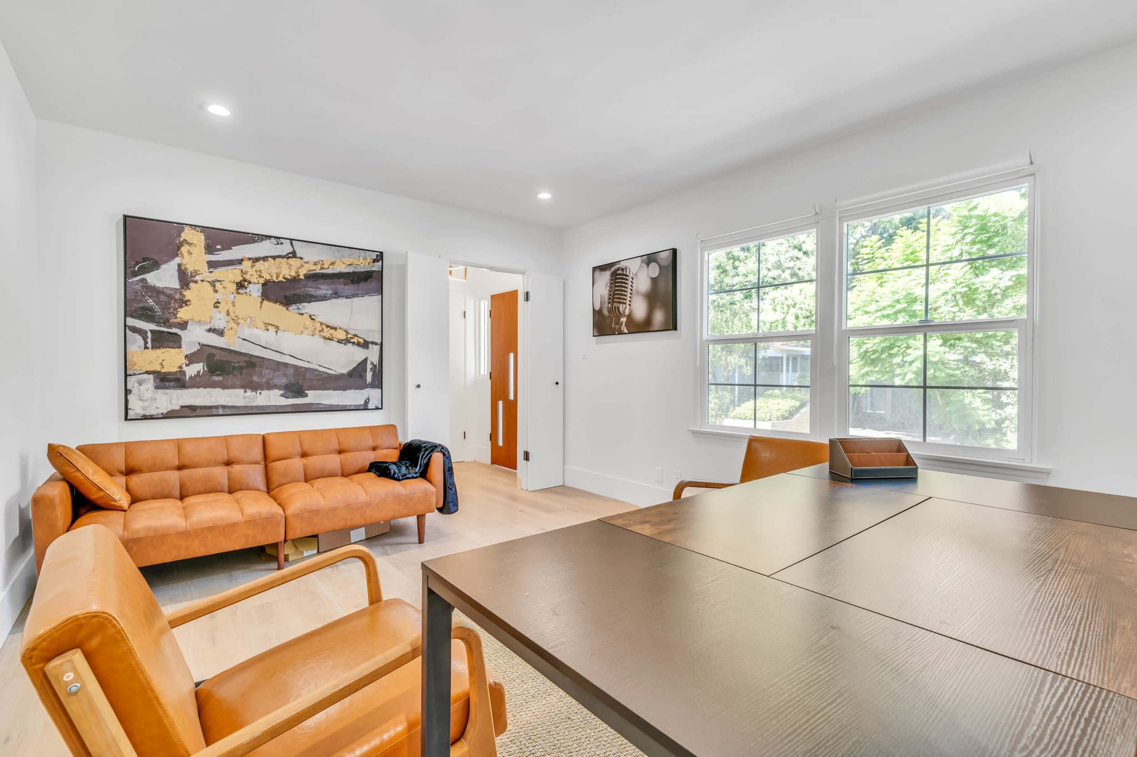 The image shows a modern interior living space featuring a brown sofa, two orange chairs, a table, and framed artwork on the walls.